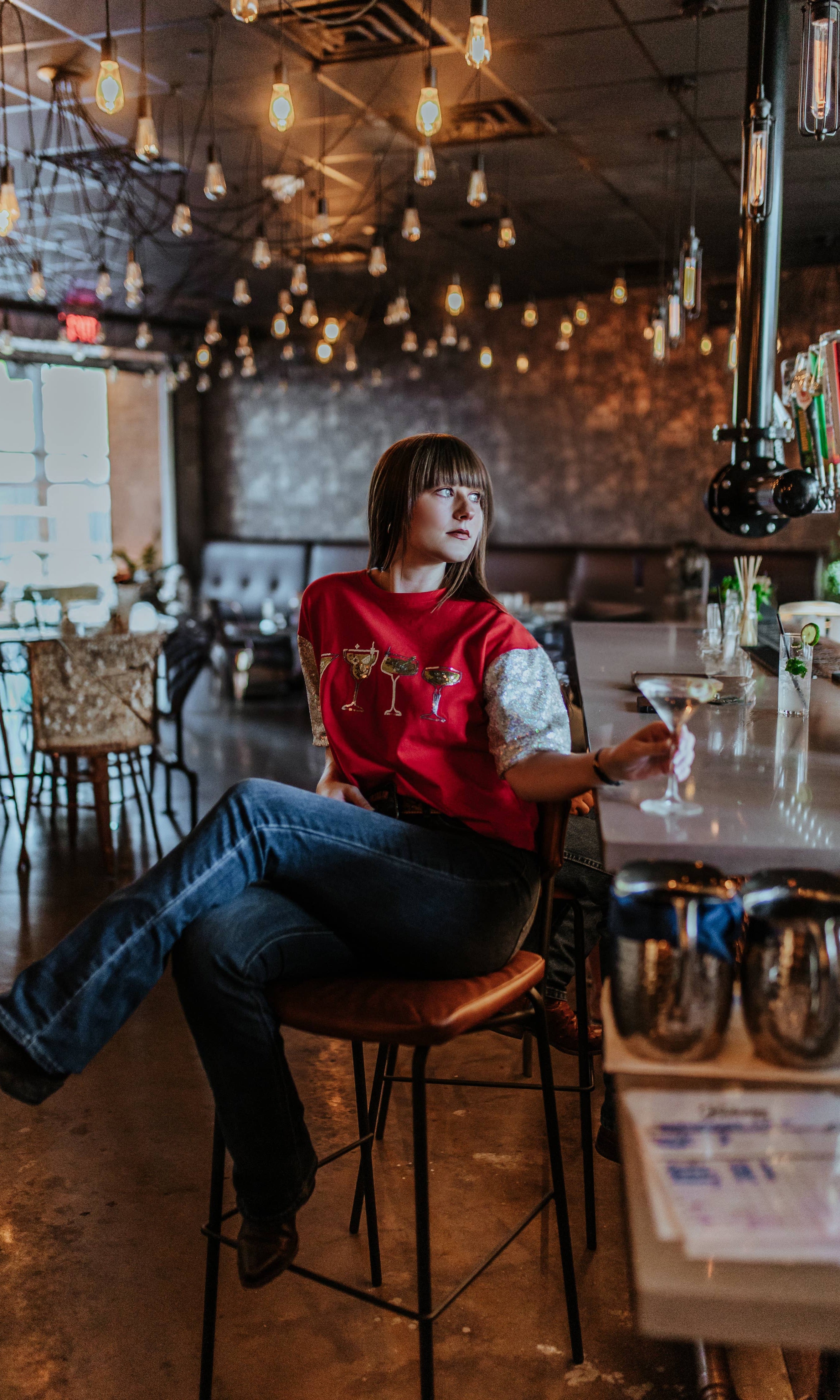 Person sitting at a bar counter in a dimly lit room with hanging lights.