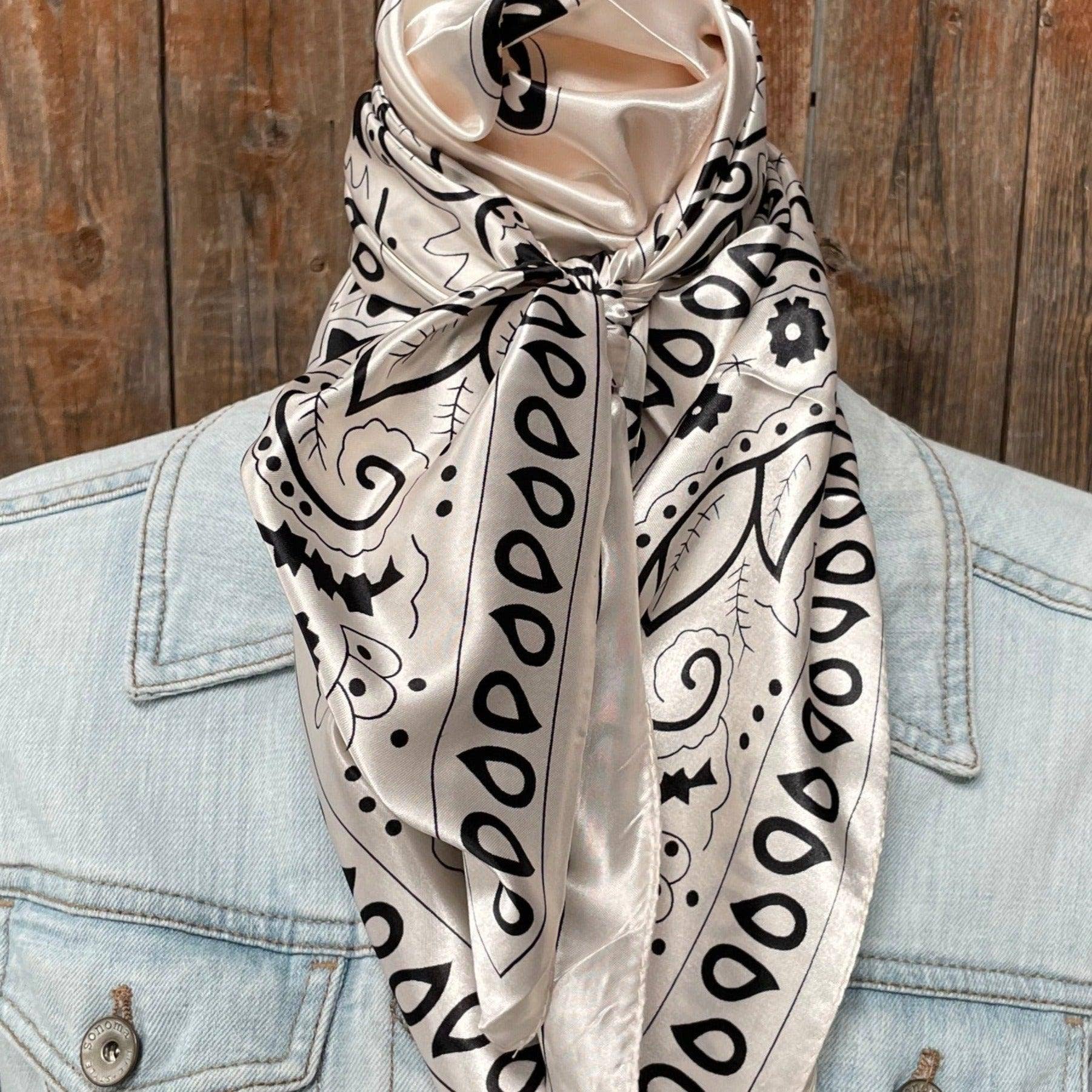 Beige scarf with black patterns draped over a light blue denim jacket against a wooden background