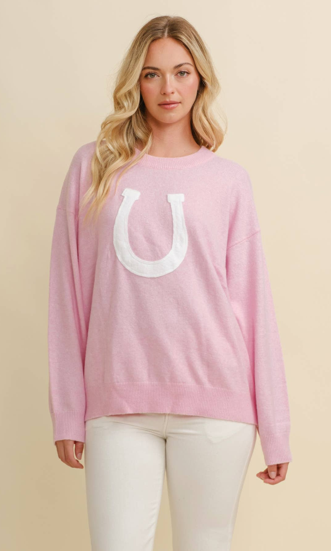 Woman wearing a pink long-sleeve shirt with a white horseshoe logo on a beige background