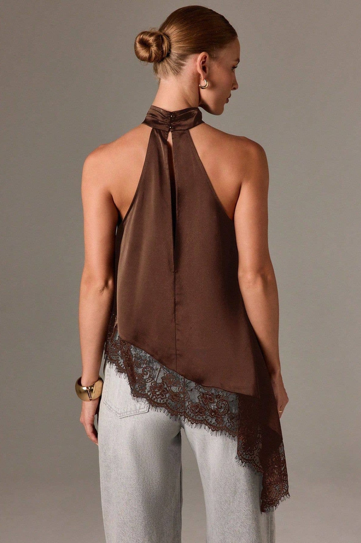 Woman wearing a brown halter top with lace trim on a plain background