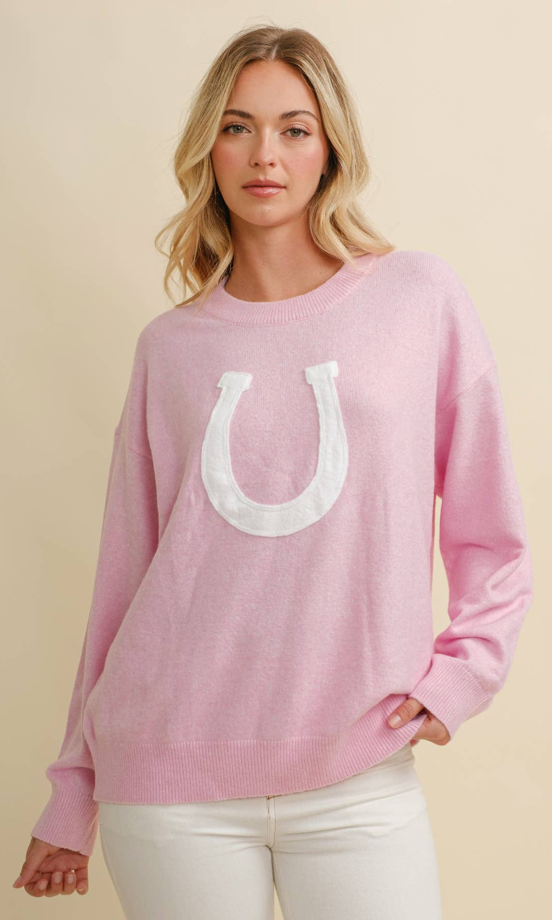 Woman wearing a pink sweatshirt with a white horseshoe design on a beige background