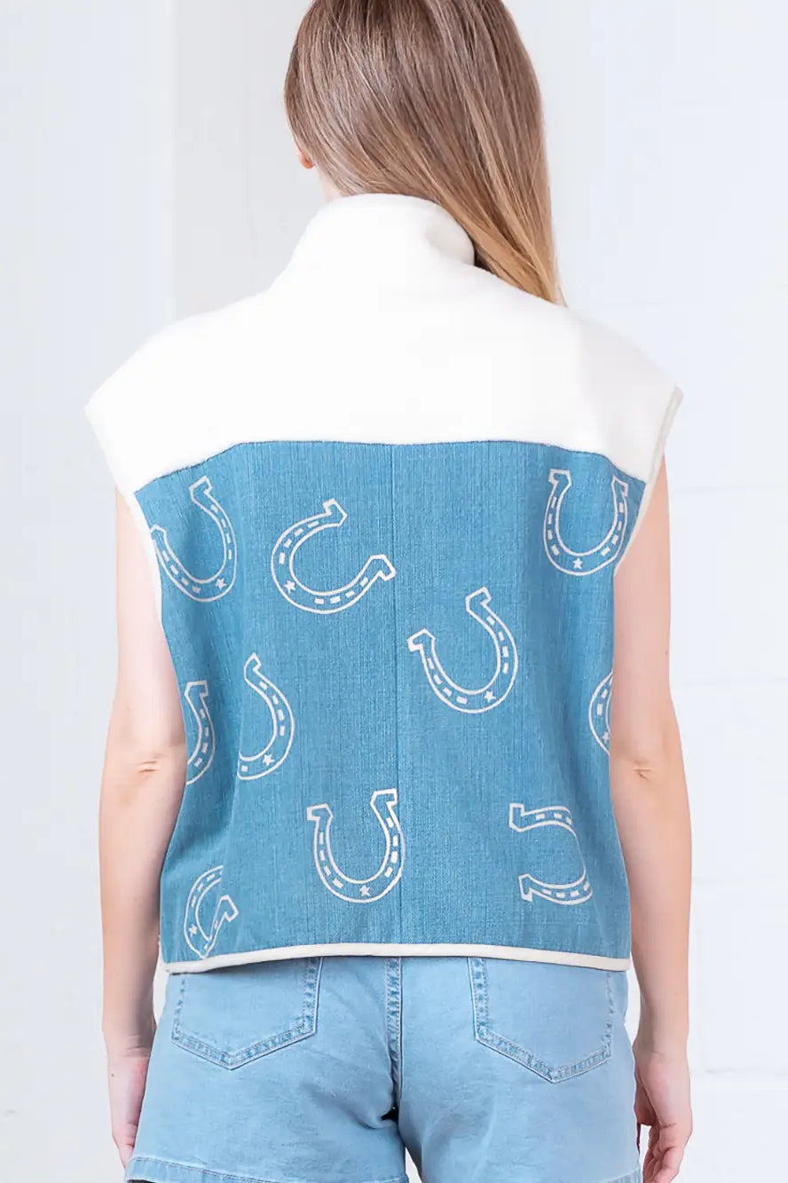 Model wearing indigo denim vest with white horseshoe print and faux-fur collar, zipped front, hands in pockets.”
