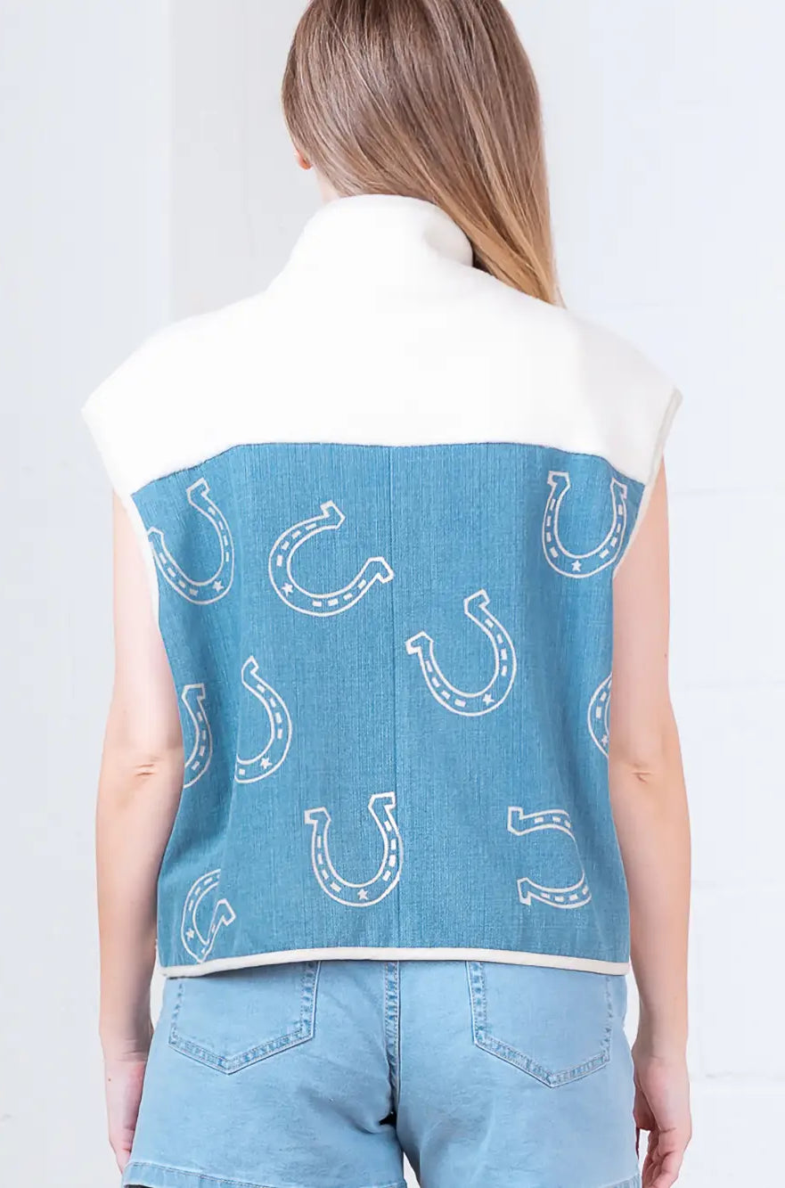 Model wearing indigo denim vest with white horseshoe print and faux-fur collar, zipped front, hands in pockets.”