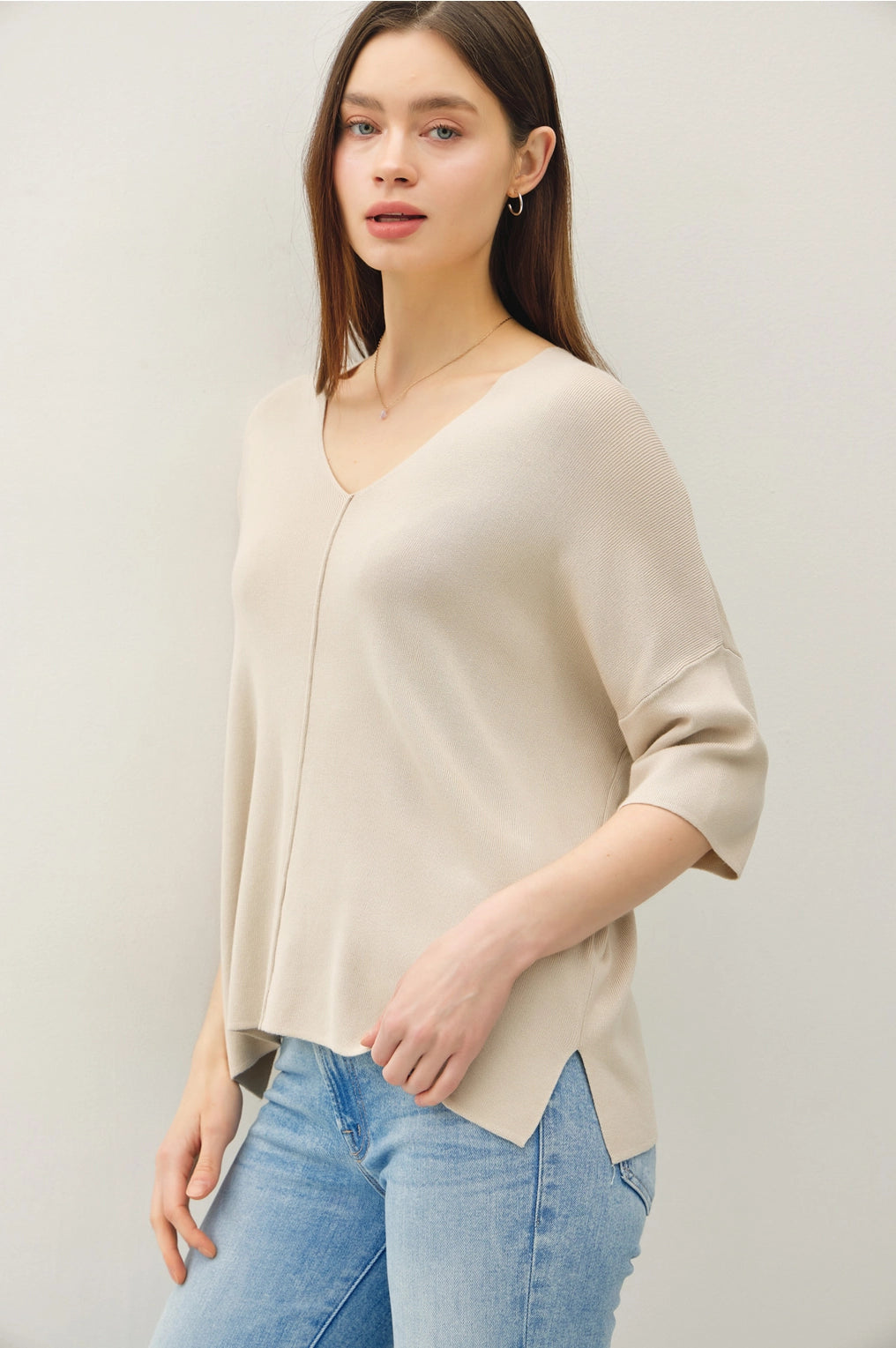 Woman wearing a beige cardigan and blue jeans against a plain background