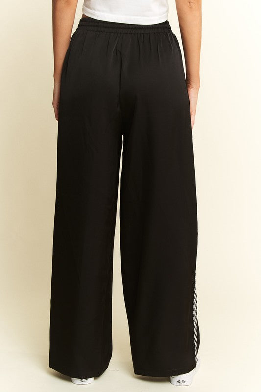 Black wide-leg pants with a side stripe on a beige background