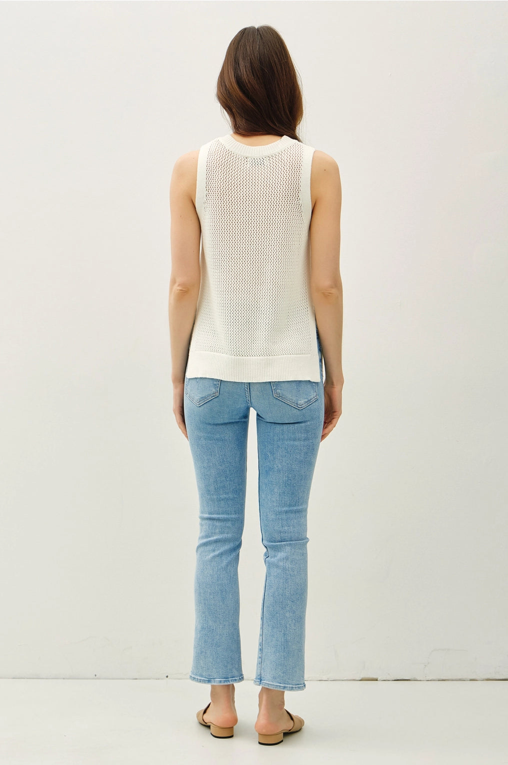 Woman wearing a white sleeveless top and light blue jeans on a plain background