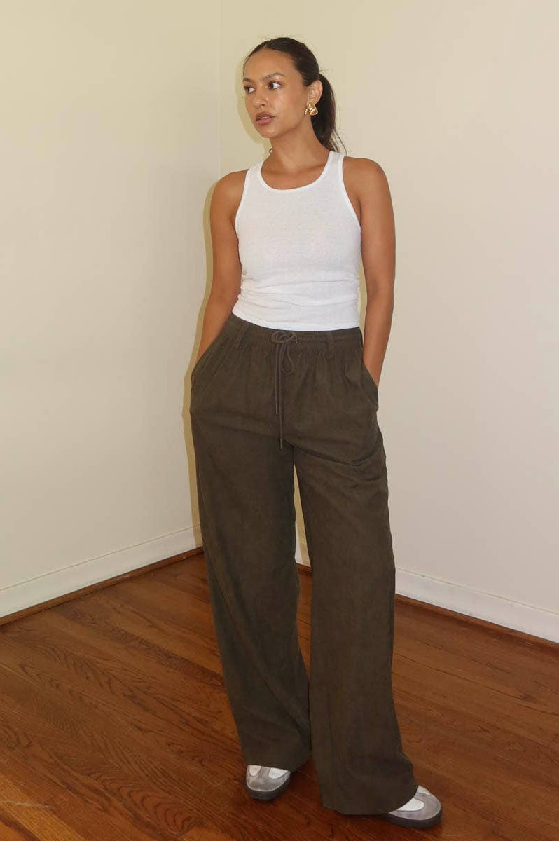 A model wearing wide leg brown pants with a drawstring waist and a white tank top.