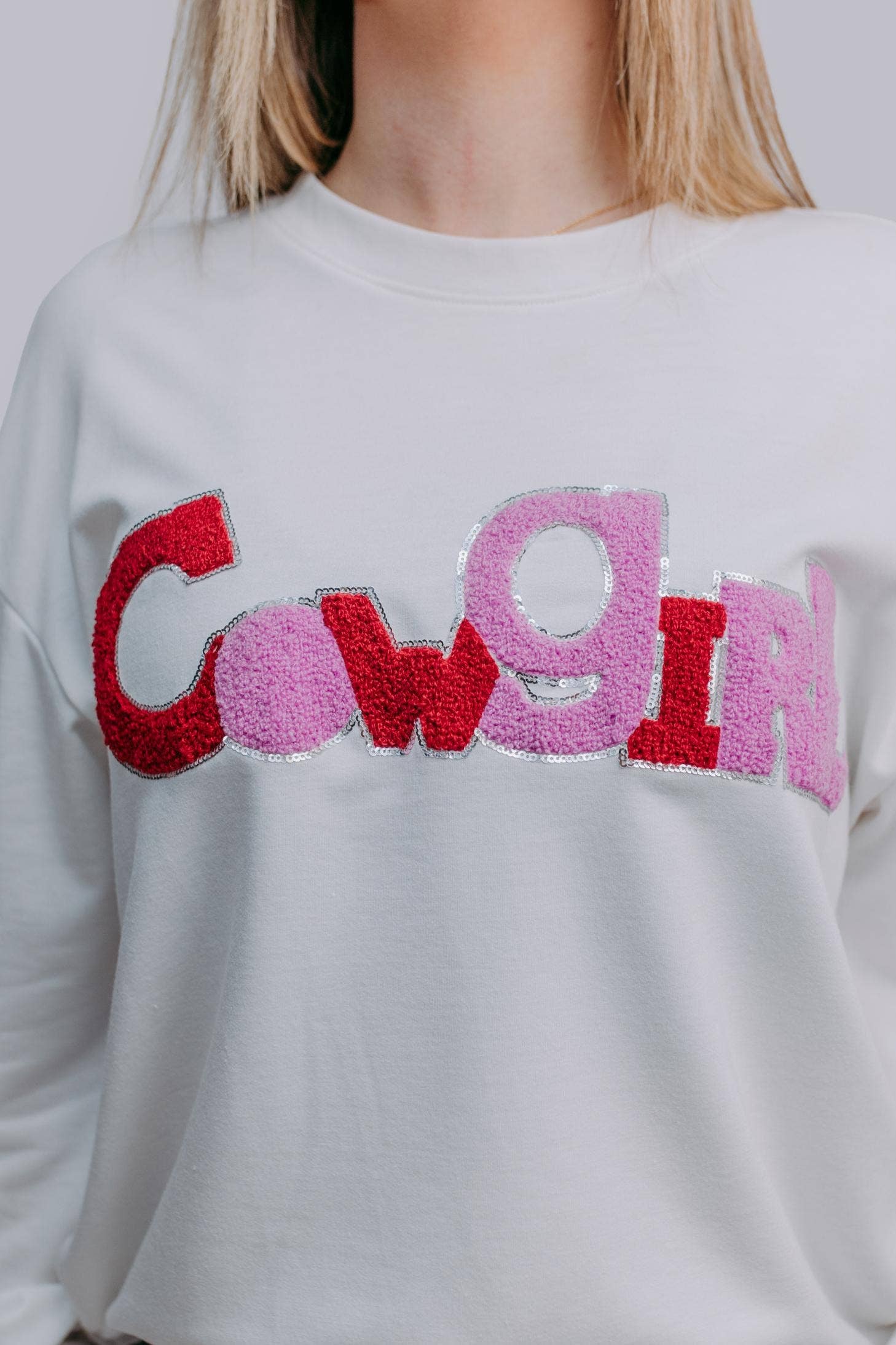 White sweatshirt with colorful letters spelling 'Cowgirl' on a plain background