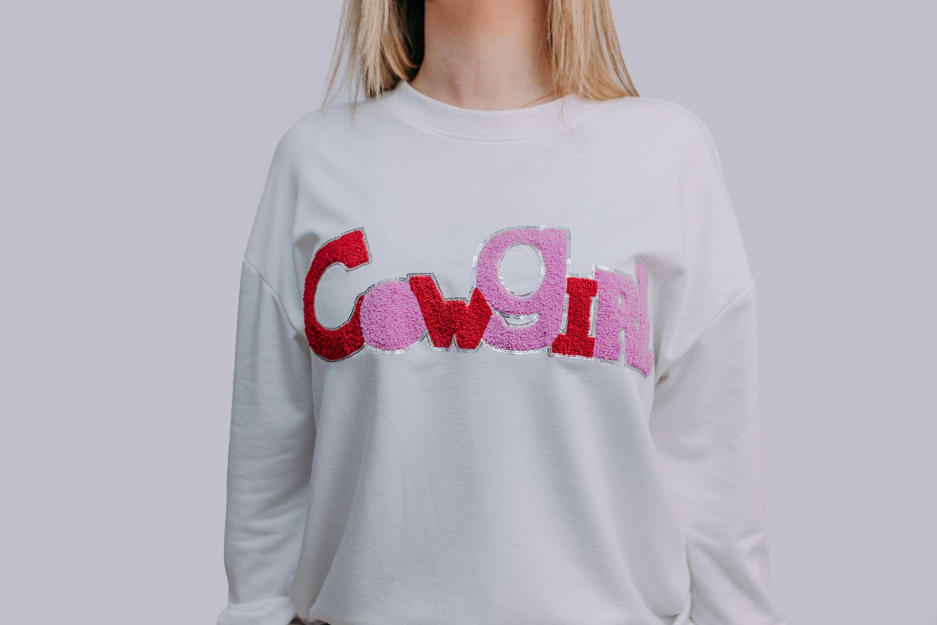 White sweatshirt with colorful letters spelling 'Cowgirl' on a plain background
