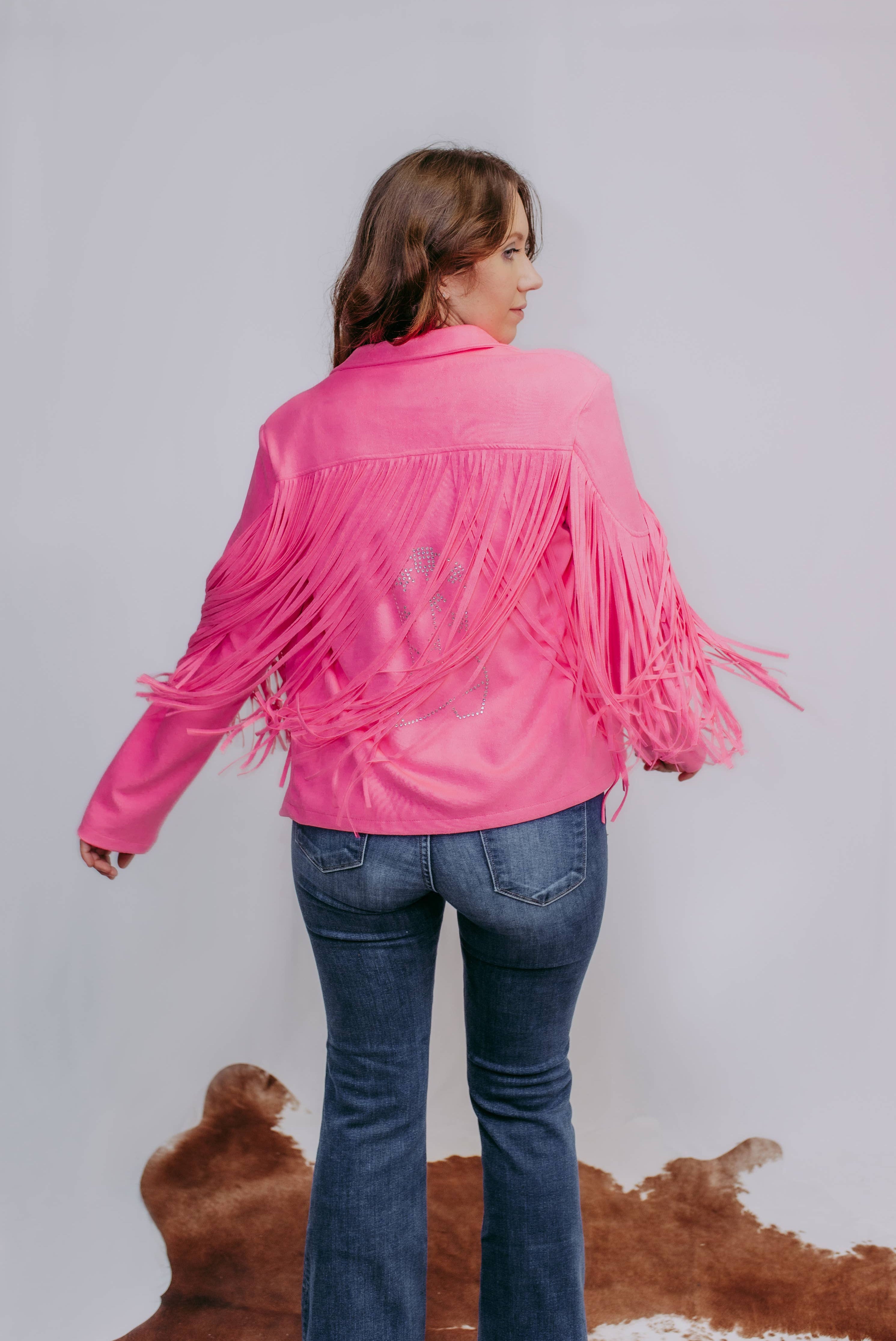Person wearing a pink fringe jacket and blue jeans against a plain background