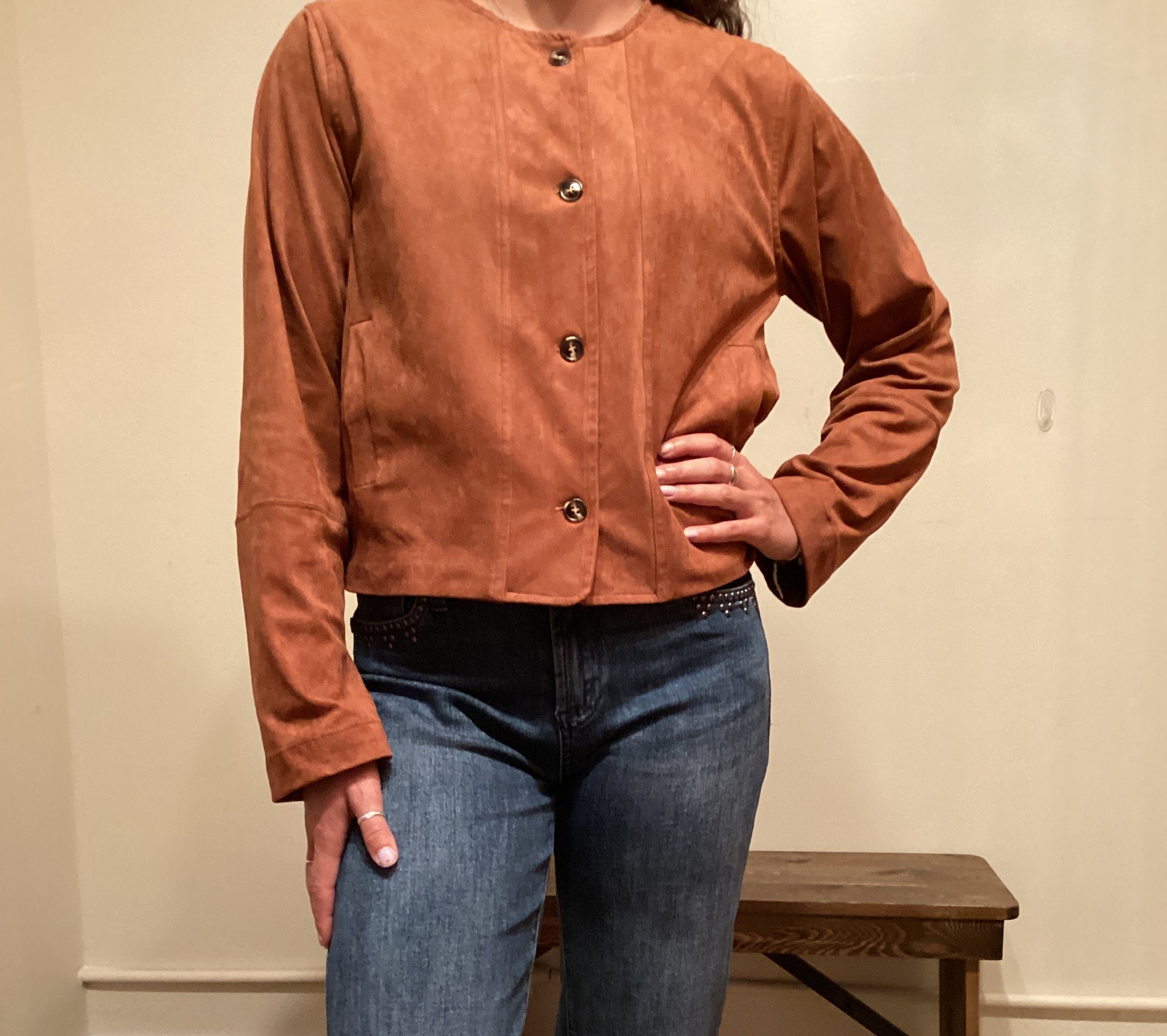 Person wearing a brown faux leather button up jacket and blue jeans