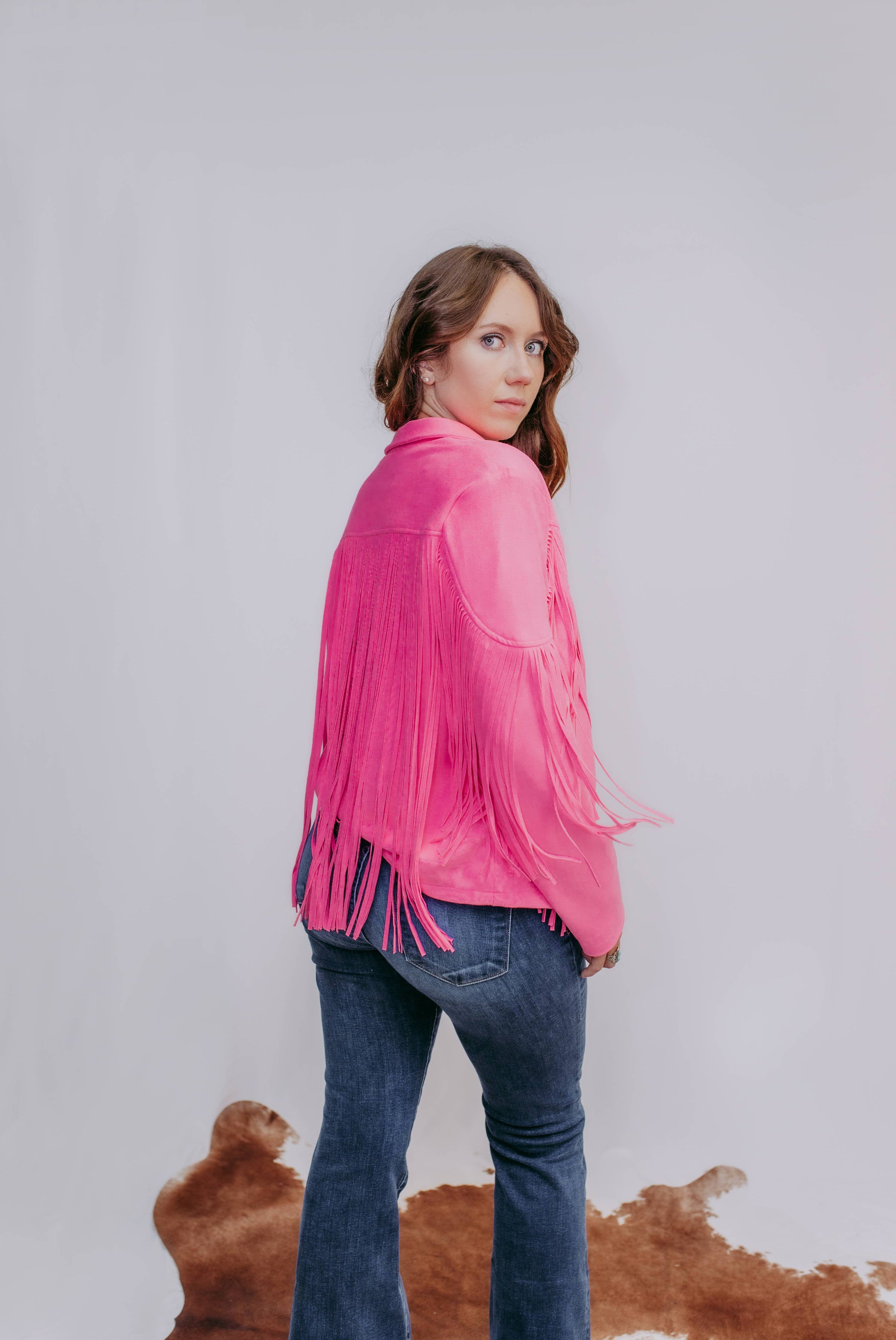 Woman wearing a pink fringed jacket and blue jeans against a plain background