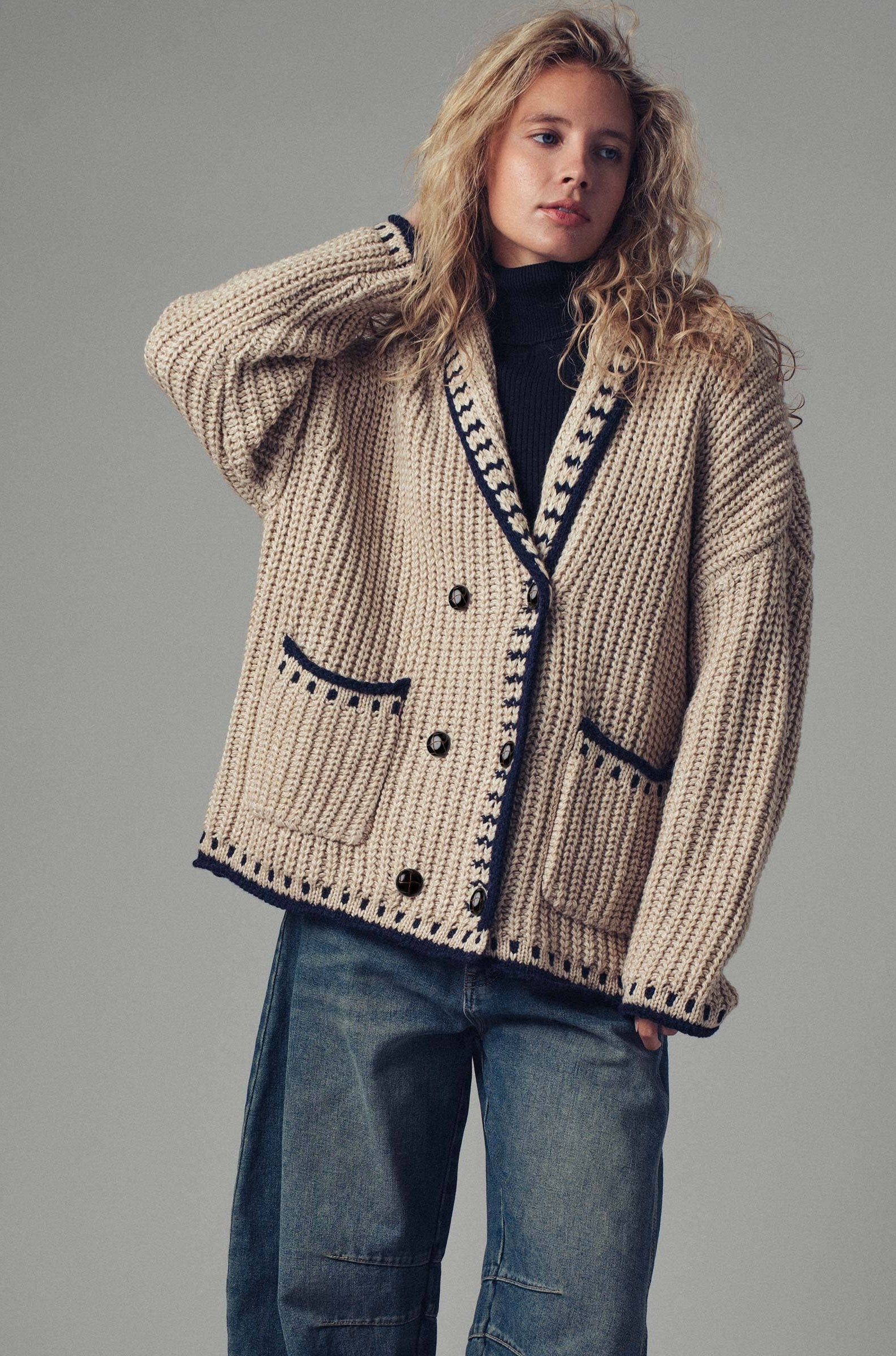 Woman wearing a beige knitted cardigan with black buttons on a gray background
