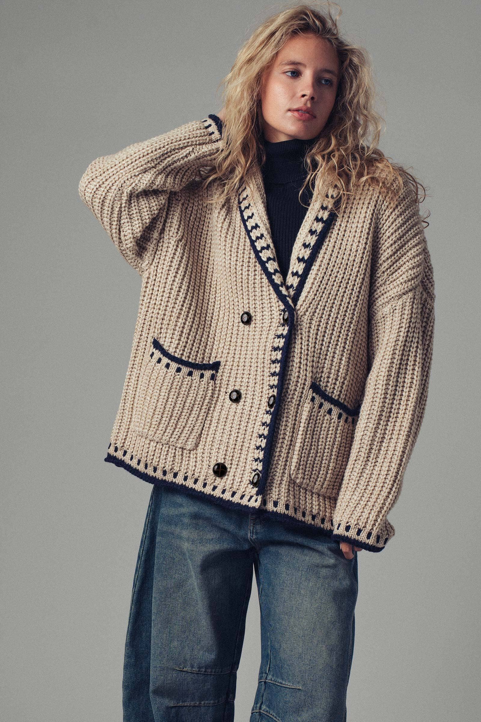 Woman wearing a beige knitted cardigan with black buttons on a gray background