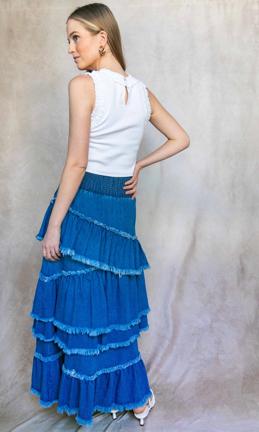 Woman wearing a white top and blue tiered skirt against a neutral background