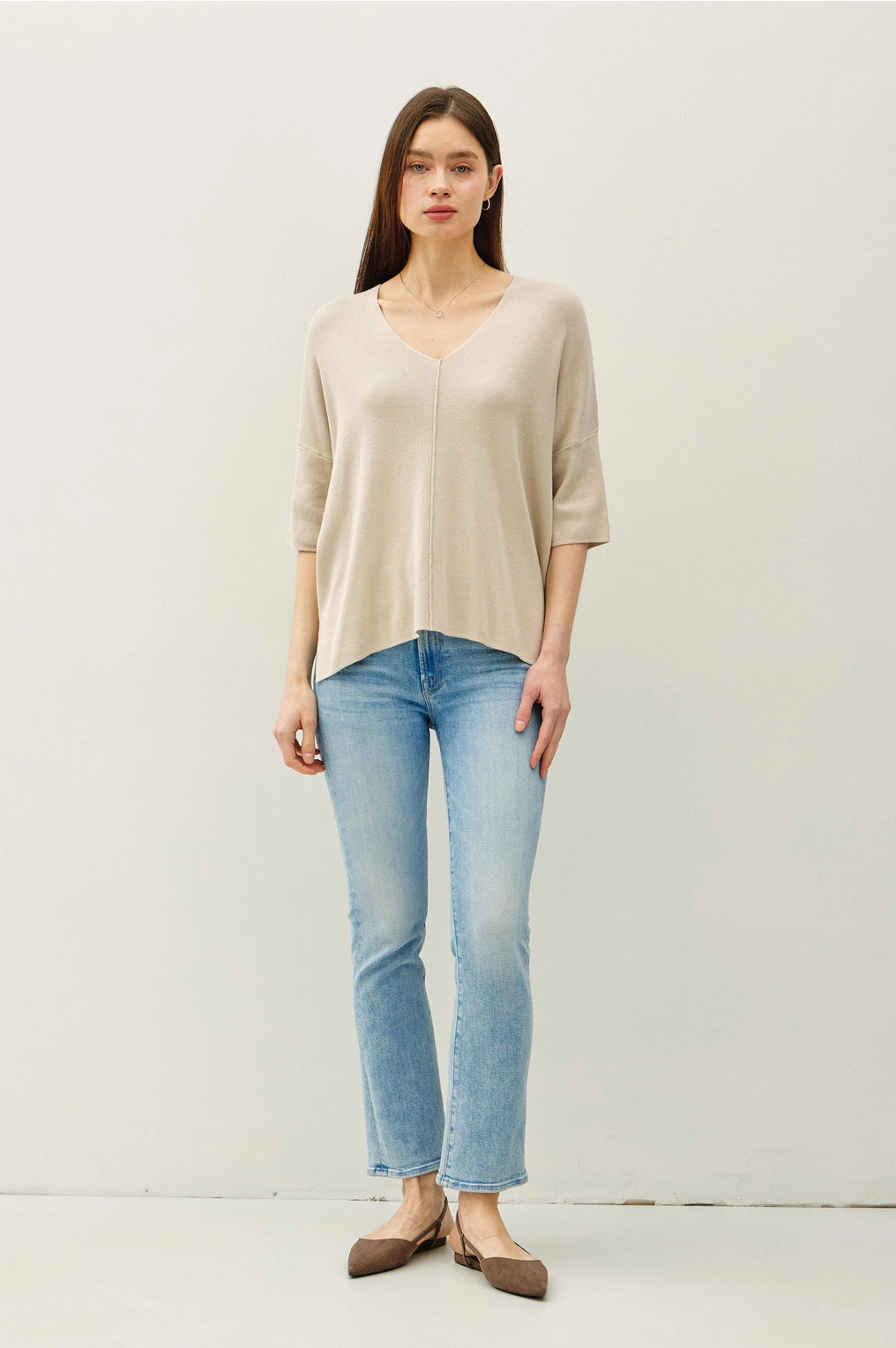 Woman wearing a beige top and light blue jeans against a white background
