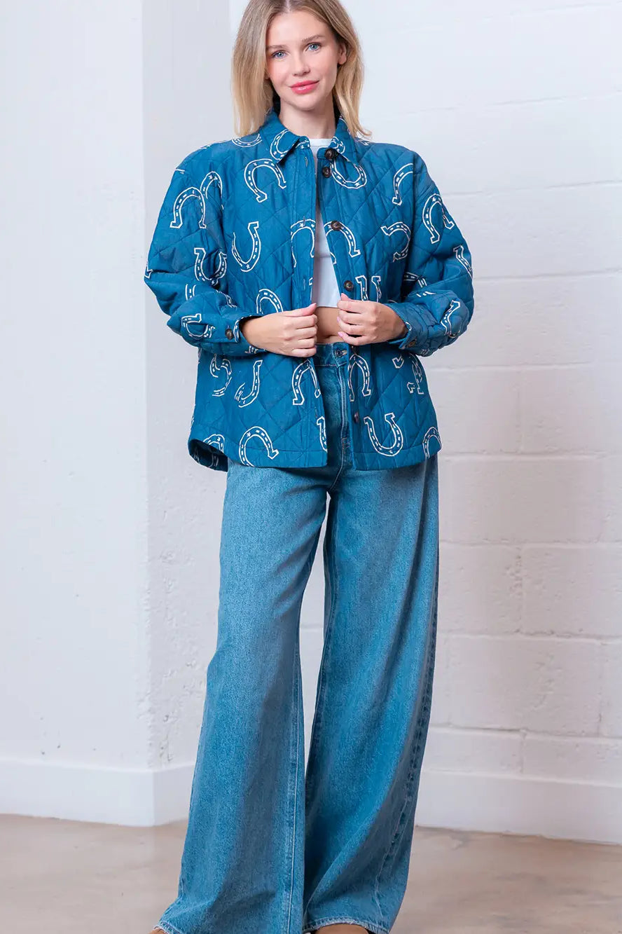 Front view of denim-blue quilted jacket with white horseshoe print and button front on model.