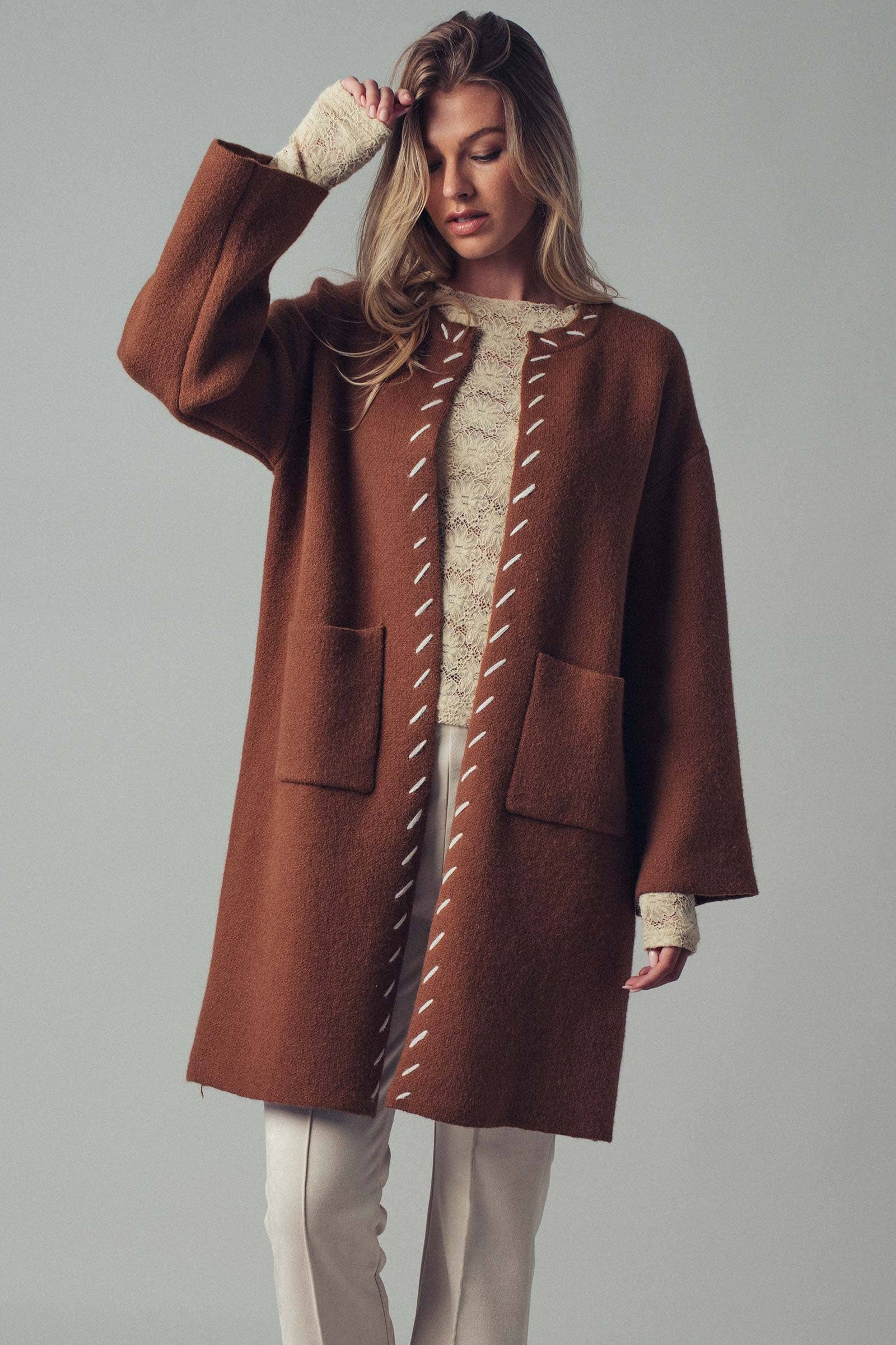 Woman wearing a brown open coat with white bold stitching trim