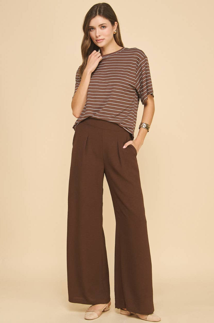 Woman wearing a striped shirt and brown wide-leg pants on a beige background