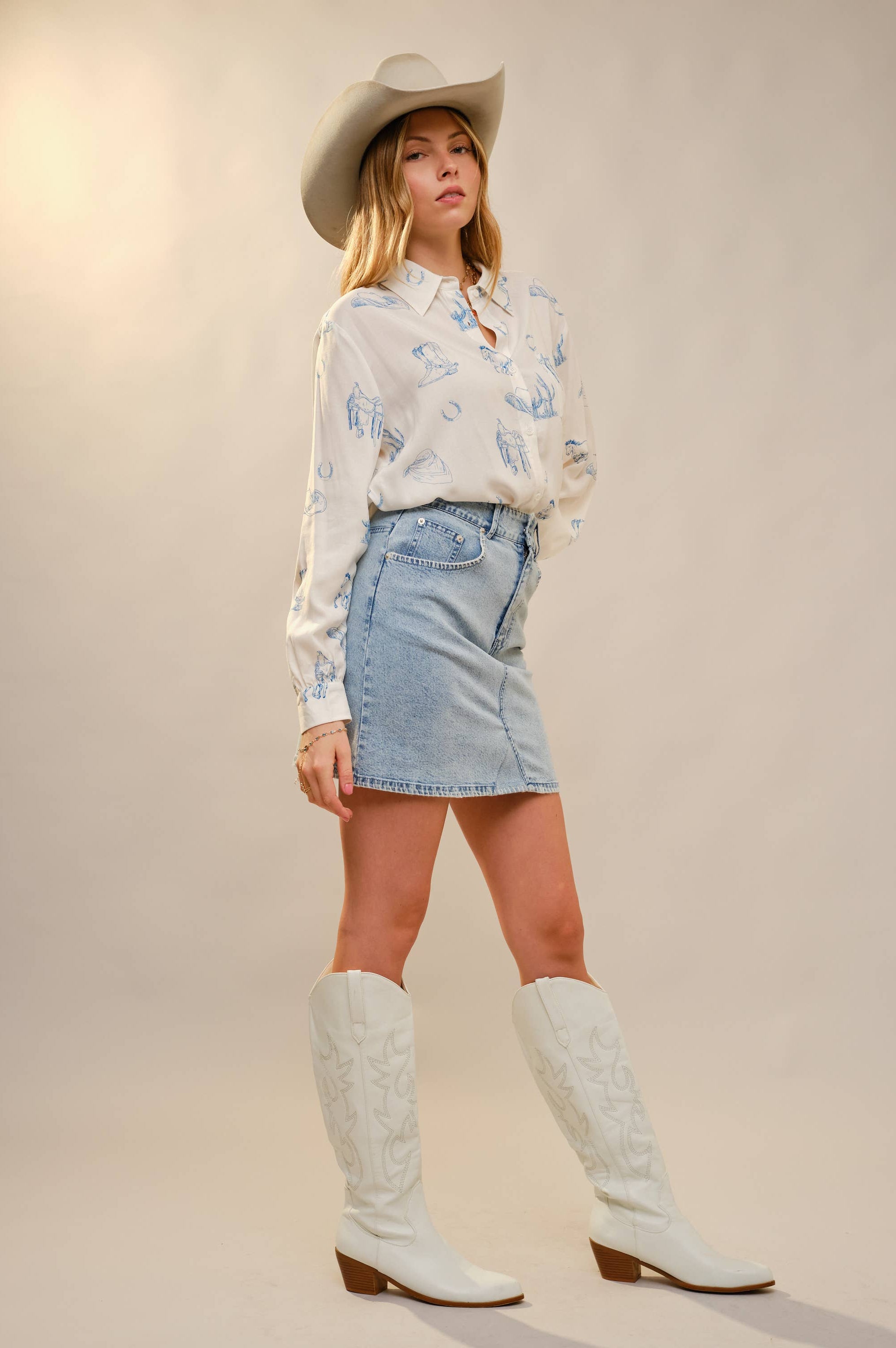 Woman wearing a floral blouse, denim skirt, and white cowboy boots on a plain background