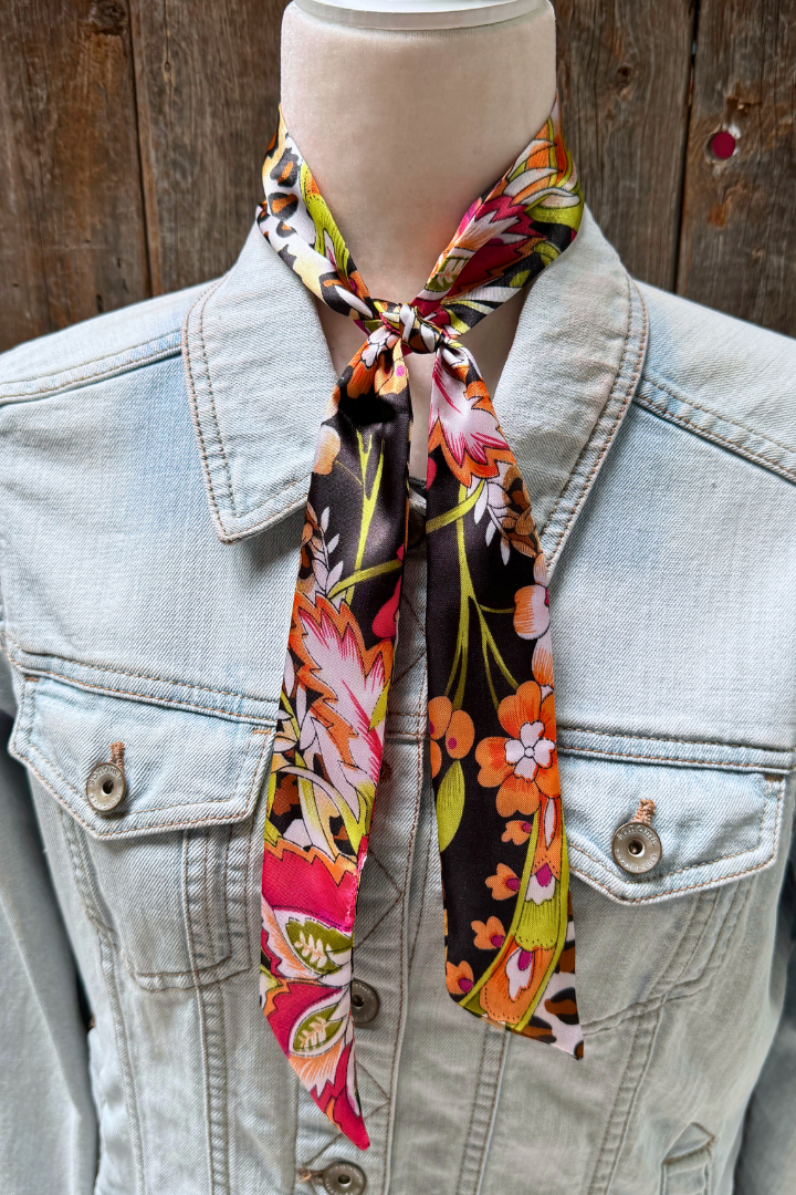Mannequin wearing a light blue denim jacket with a colorful floral scarf draped over the neck against a wooden background.