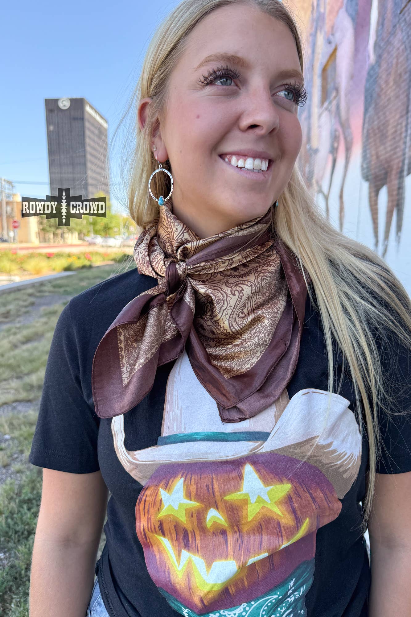 Woman wearing a black t-shirt with a pumpkin design and a brown scarf, standing outdoors.