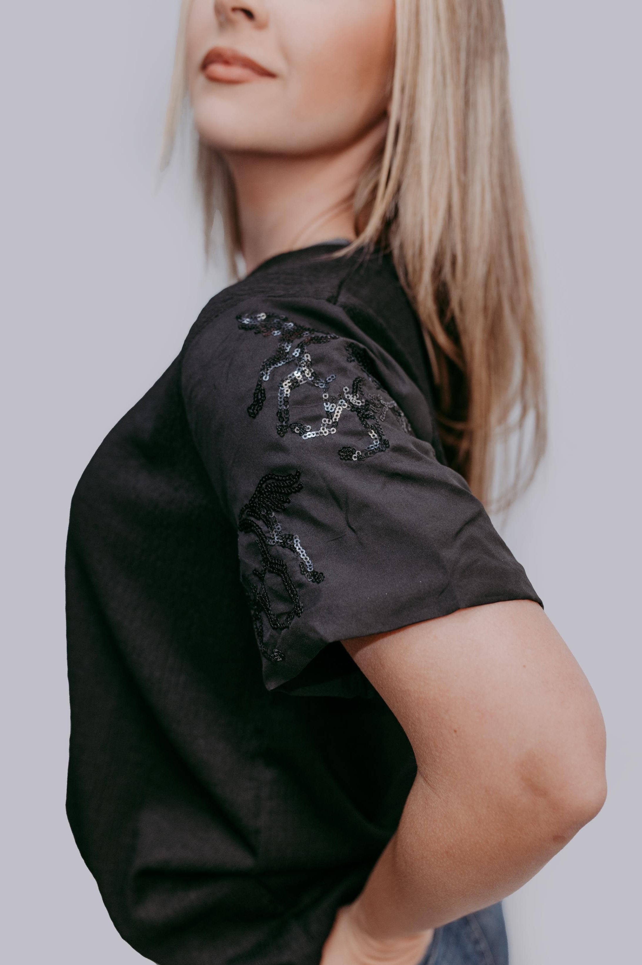 Person wearing a black t-shirt with sequin horse details on a plain background