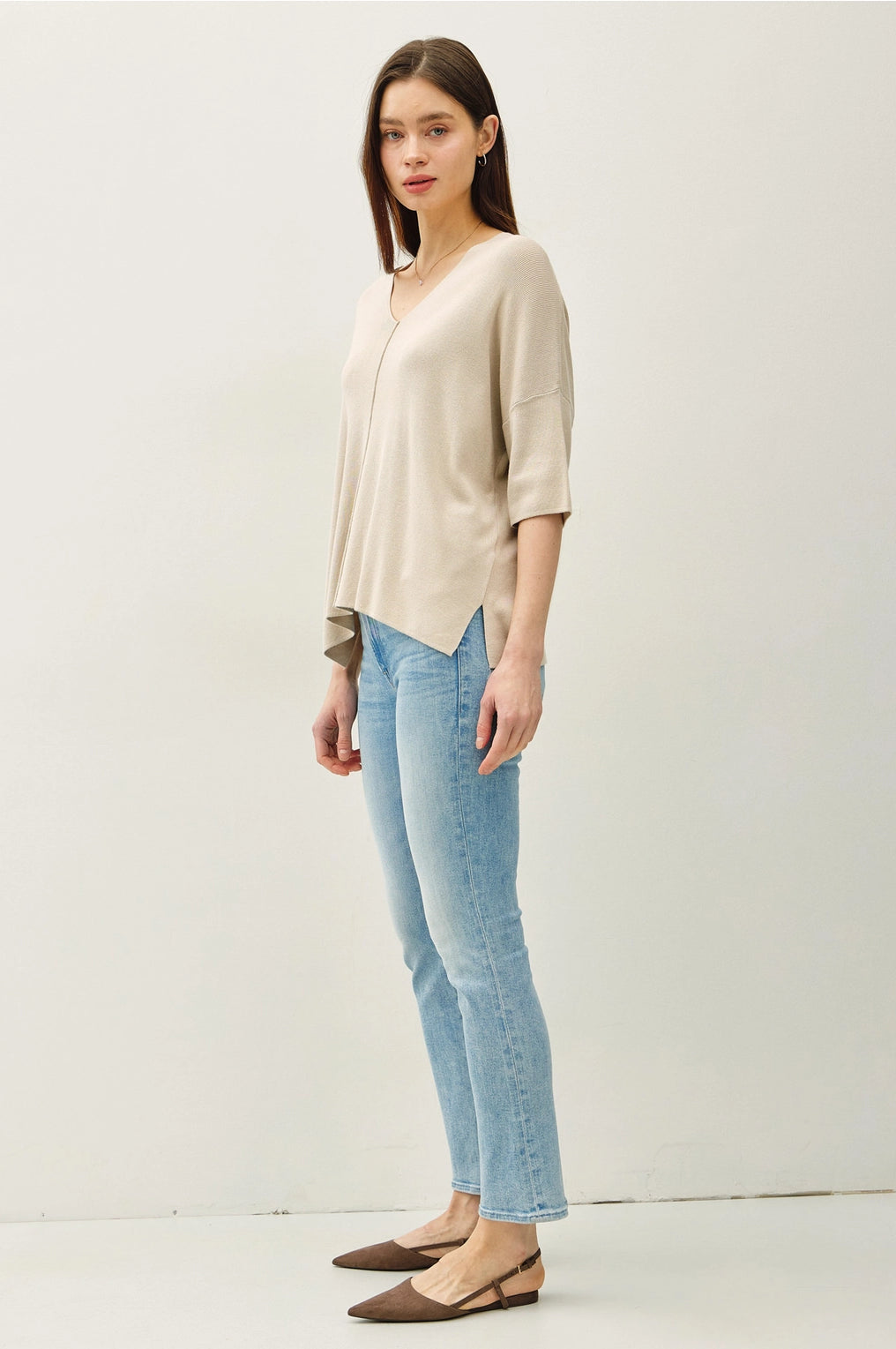 Woman wearing a beige cardigan, light blue jeans, and brown shoes on a white background