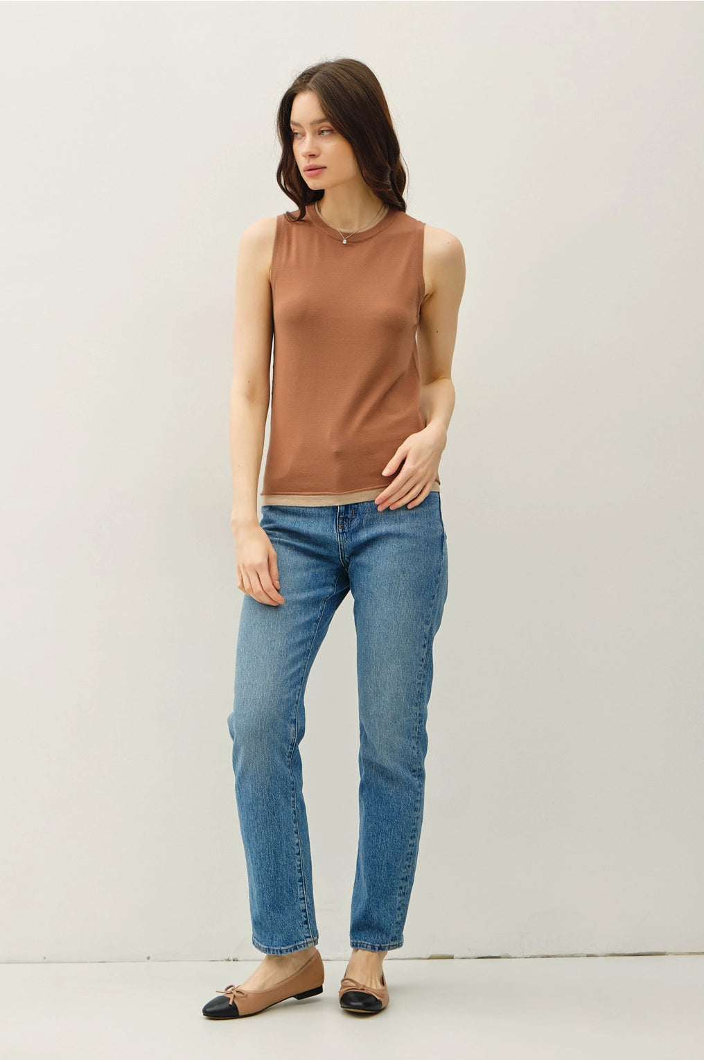 Woman wearing a brown sleeveless top and blue jeans against a white background