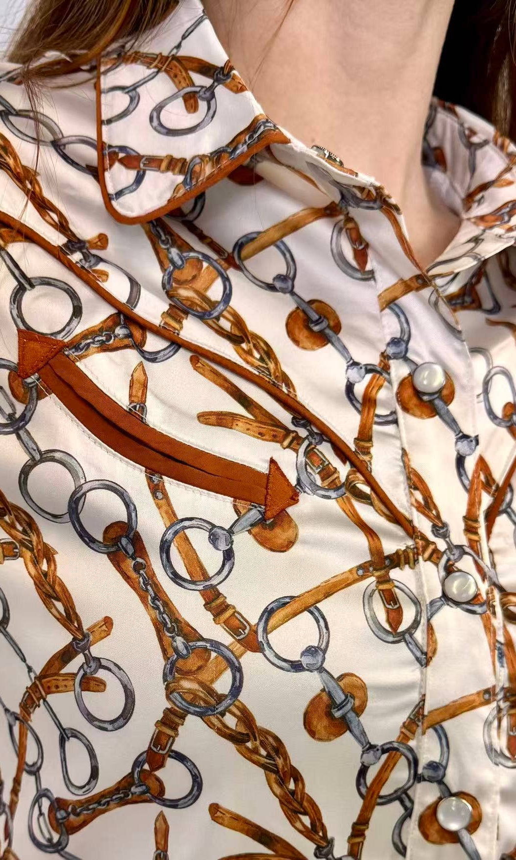 Close-up of a shirt with a pattern of brown horsewhips and silver rings on a white background.