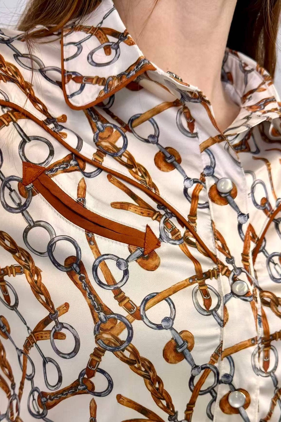 Close-up of a shirt with a pattern of brown horsewhips and silver rings on a white background.
