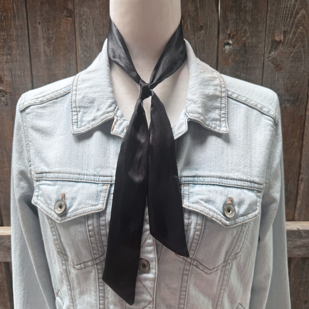 Light denim jacket with a black scarf around the neck against a wooden background
