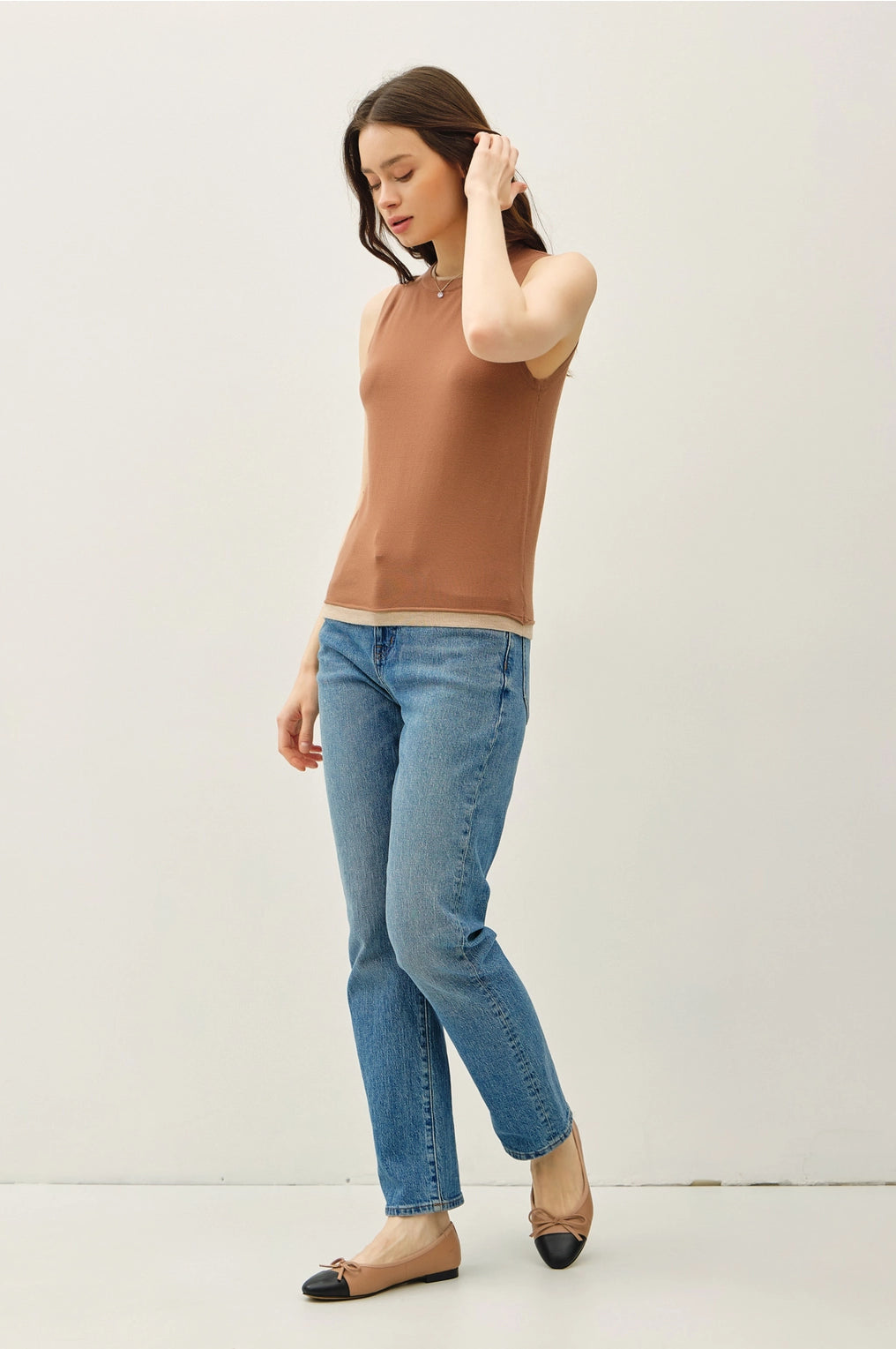 Woman wearing a brown sleeveless top and blue jeans on a white background