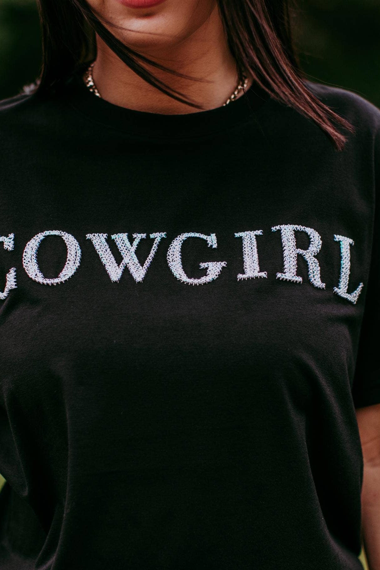 Person wearing a black t-shirt with 'COWGIRL' text in a field