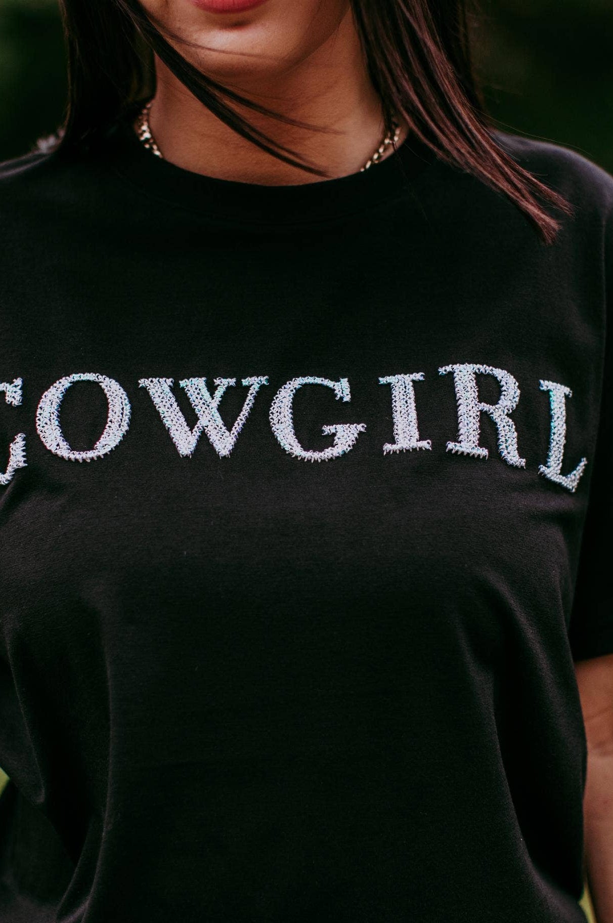 Person wearing a black t-shirt with 'COWGIRL' text in a field