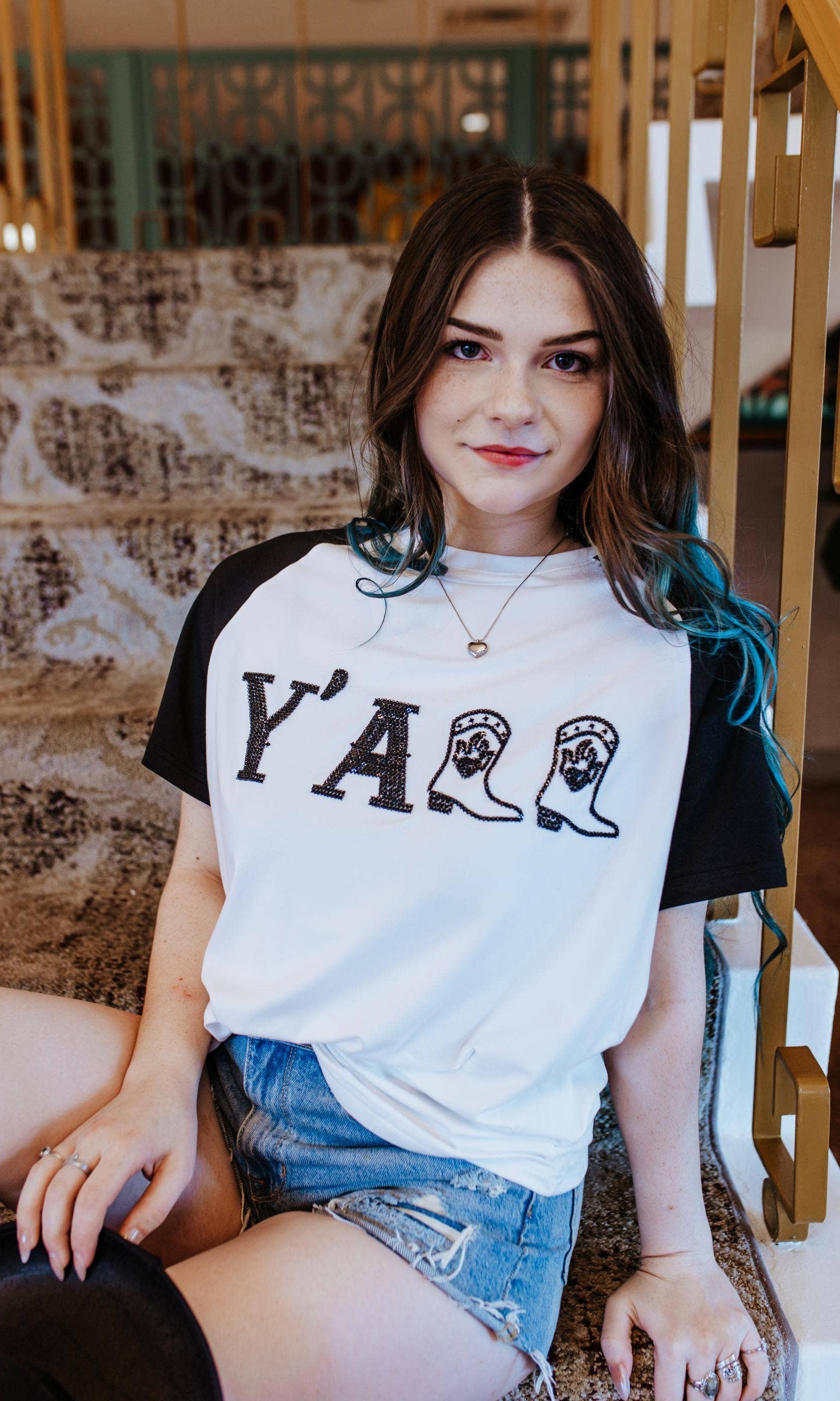 Woman wearing a white t-shirt with 'Y'ALL' printed on it, sitting on a staircase.