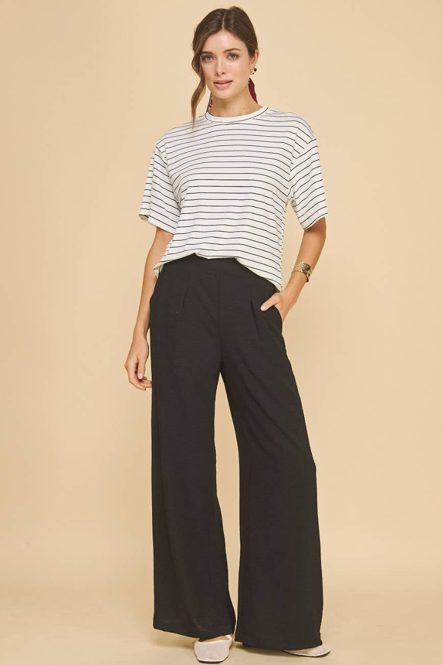 Woman wearing a striped shirt and black wide-leg pants on a beige background