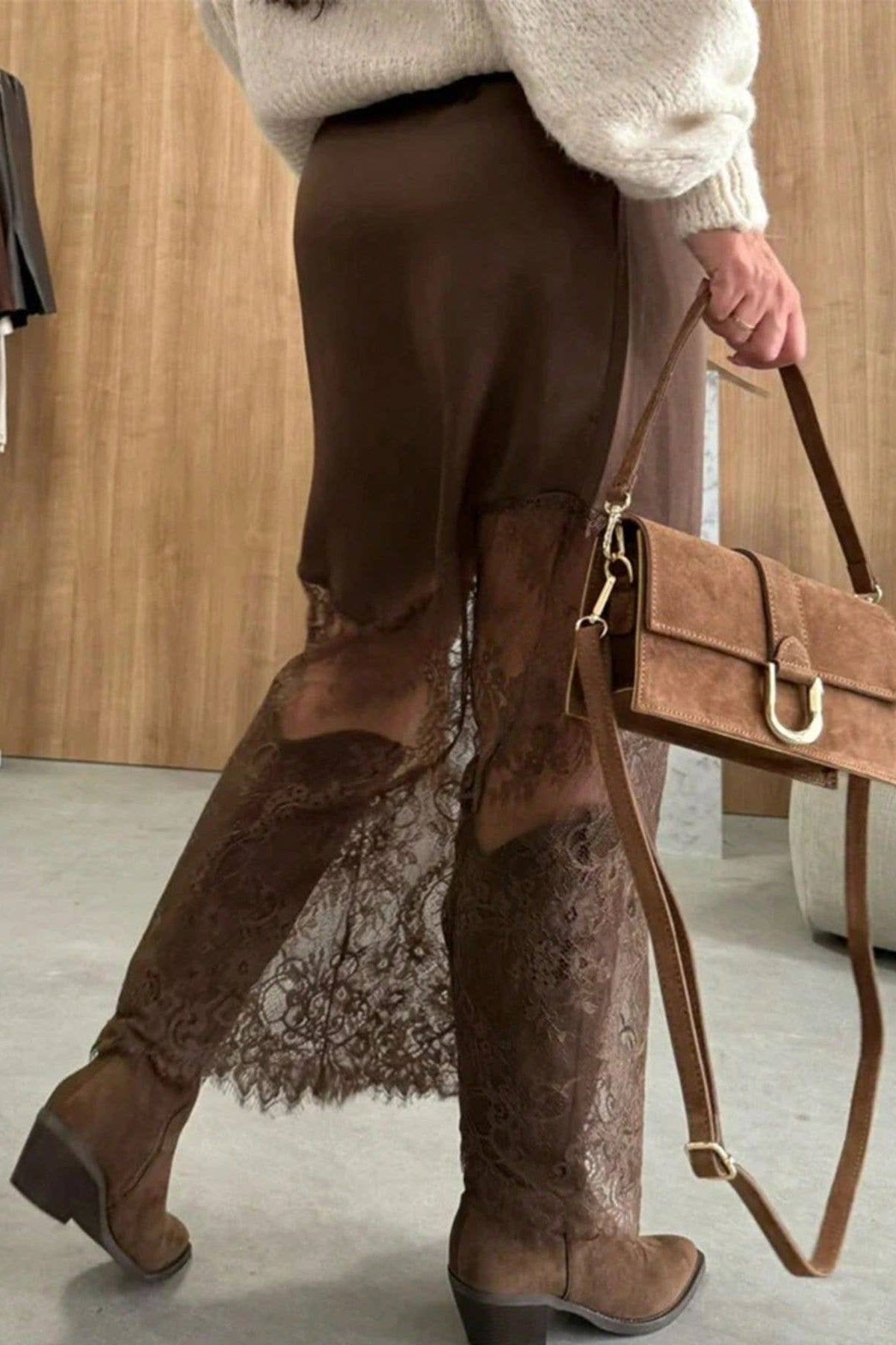 Person wearing brown lace pants and boots, holding a matching brown handbag.