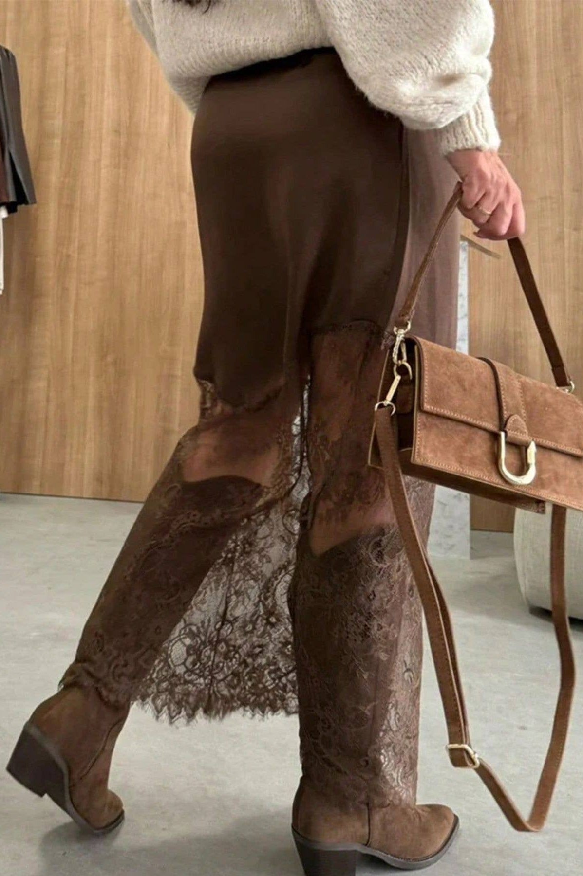 Person wearing brown lace pants and boots, holding a matching brown handbag.