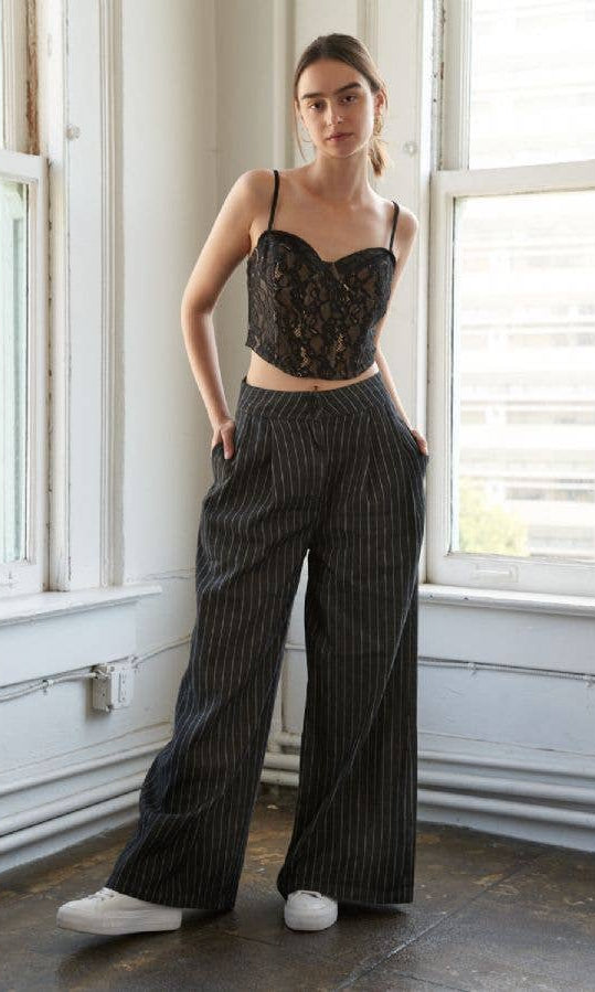 Woman wearing a black lace cropped top and wide-leg pants in a room with large windows.