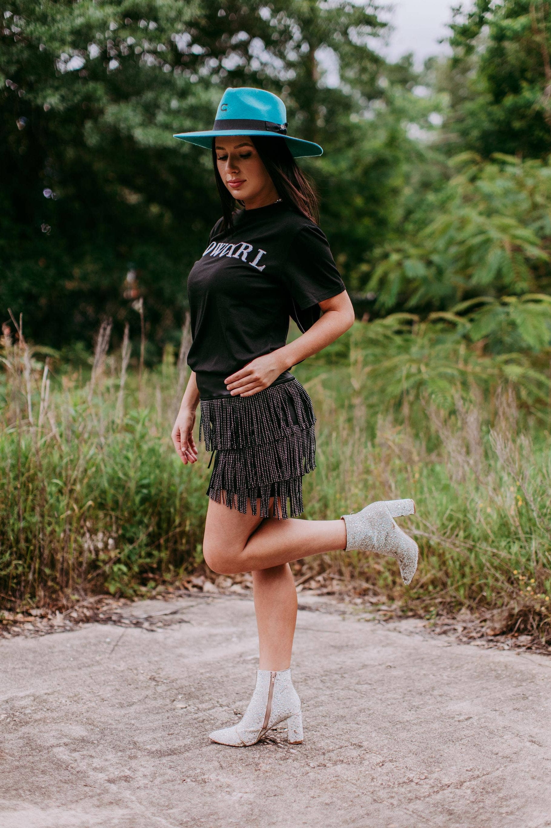 Woman in a black outfit with a blue hat standing outdoors in a natural setting