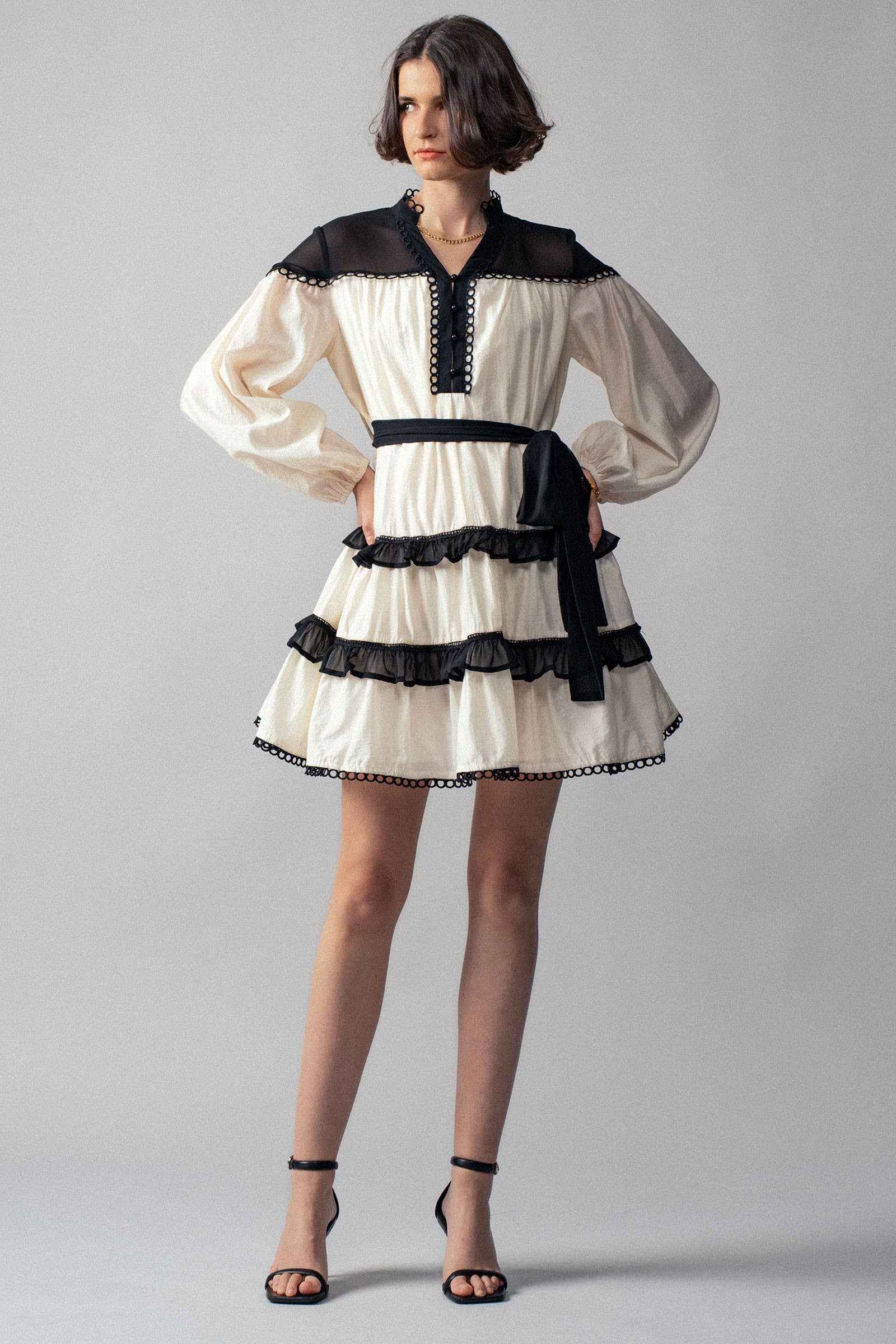 Woman wearing a white dress with black ruffle accents on a gray background