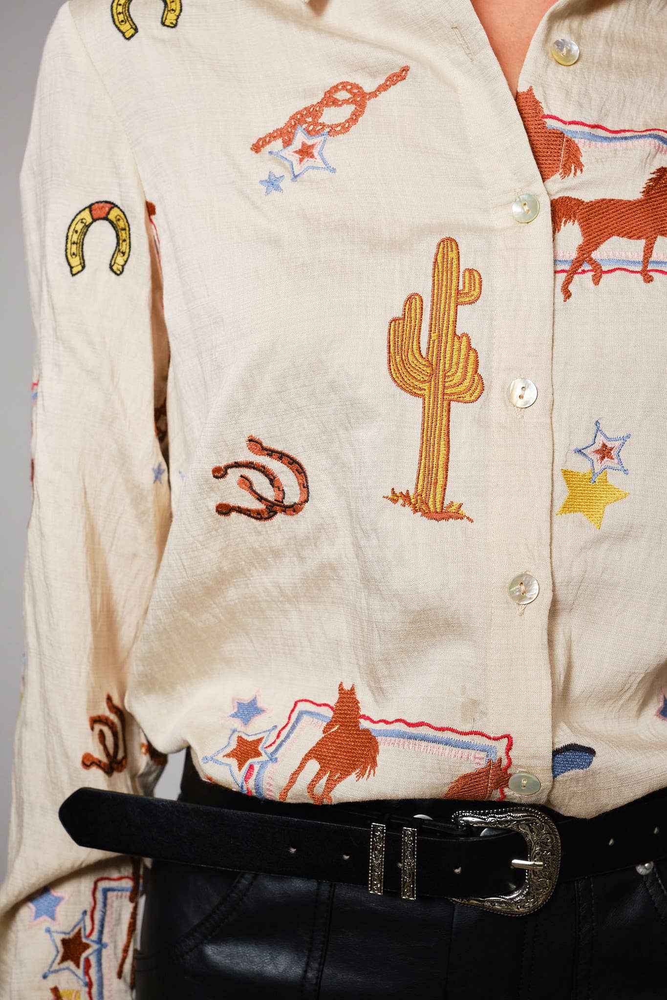 Close-up of a person wearing a cream-colored shirt with embroidered western designs.