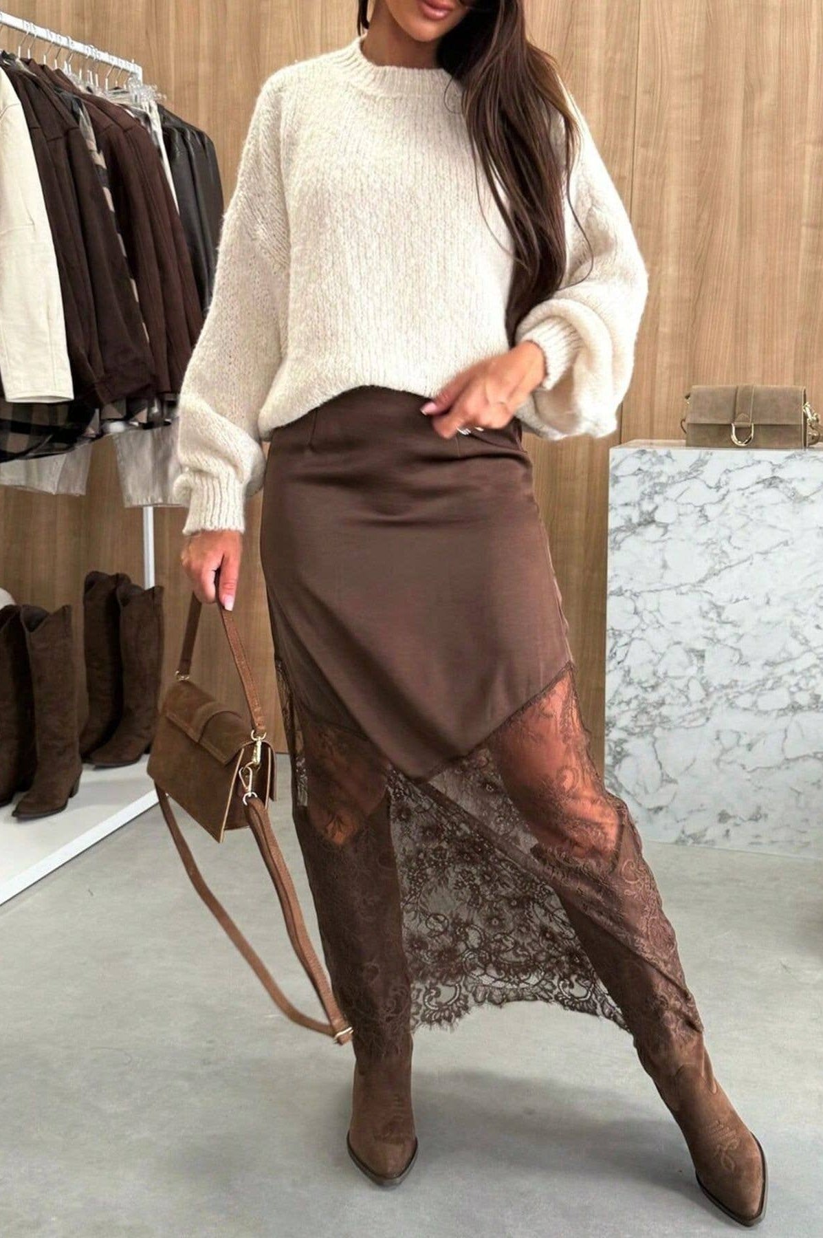 Woman wearing a beige sweater and brown skirt with lace overlay in a clothing store.