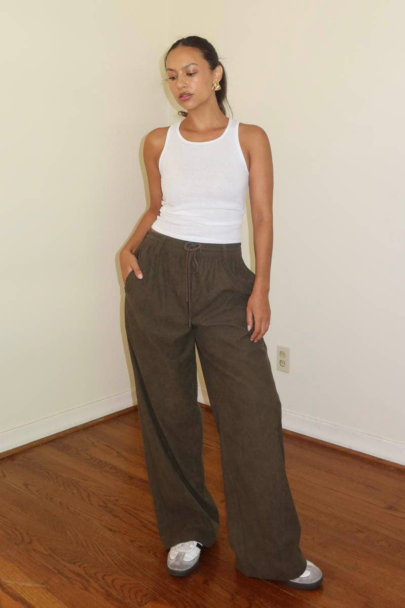 Woman in white tank top and brown wide-leg pants standing indoors.
