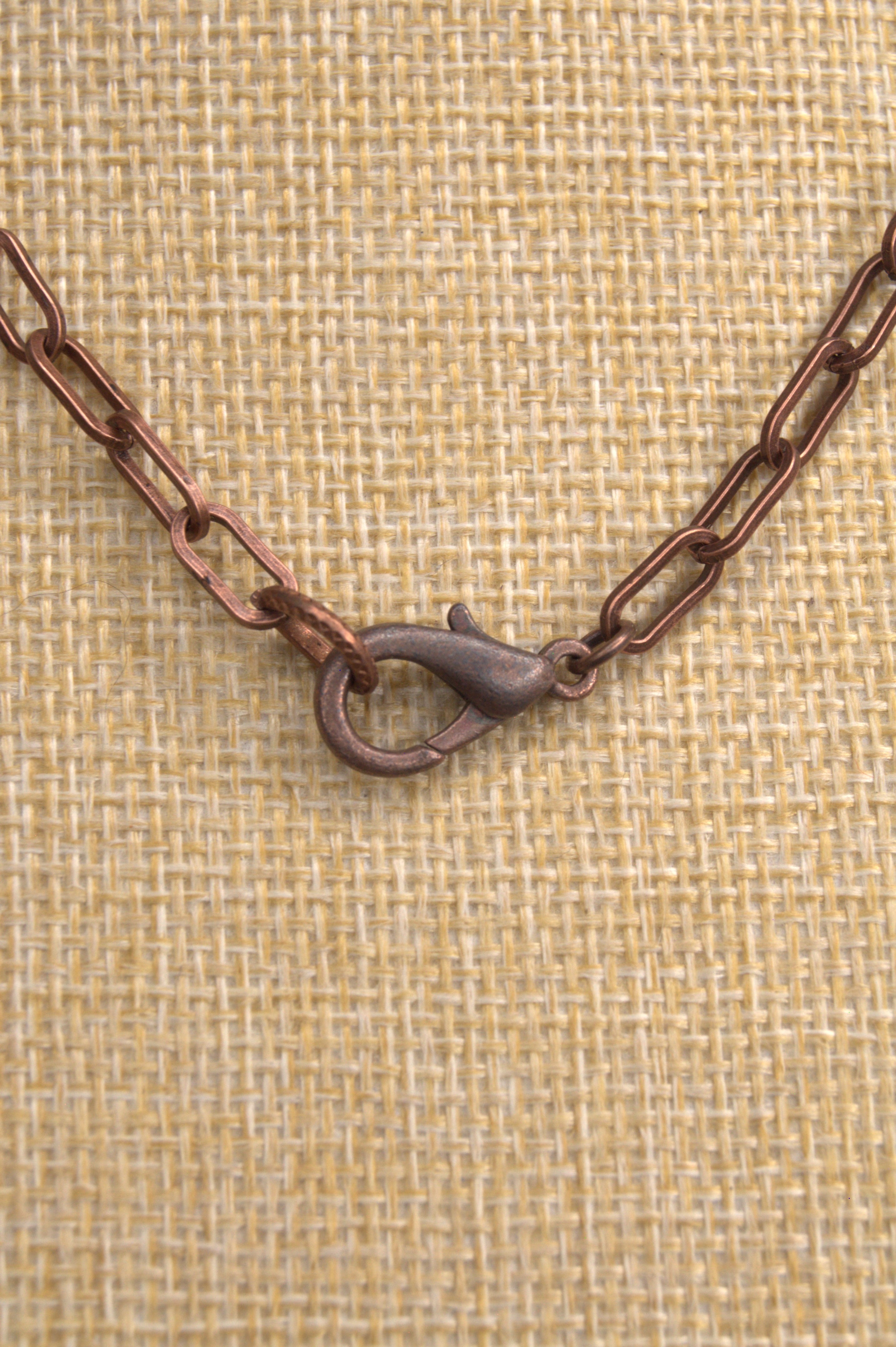 Close-up of a copper chain with a clasp on a textured beige background