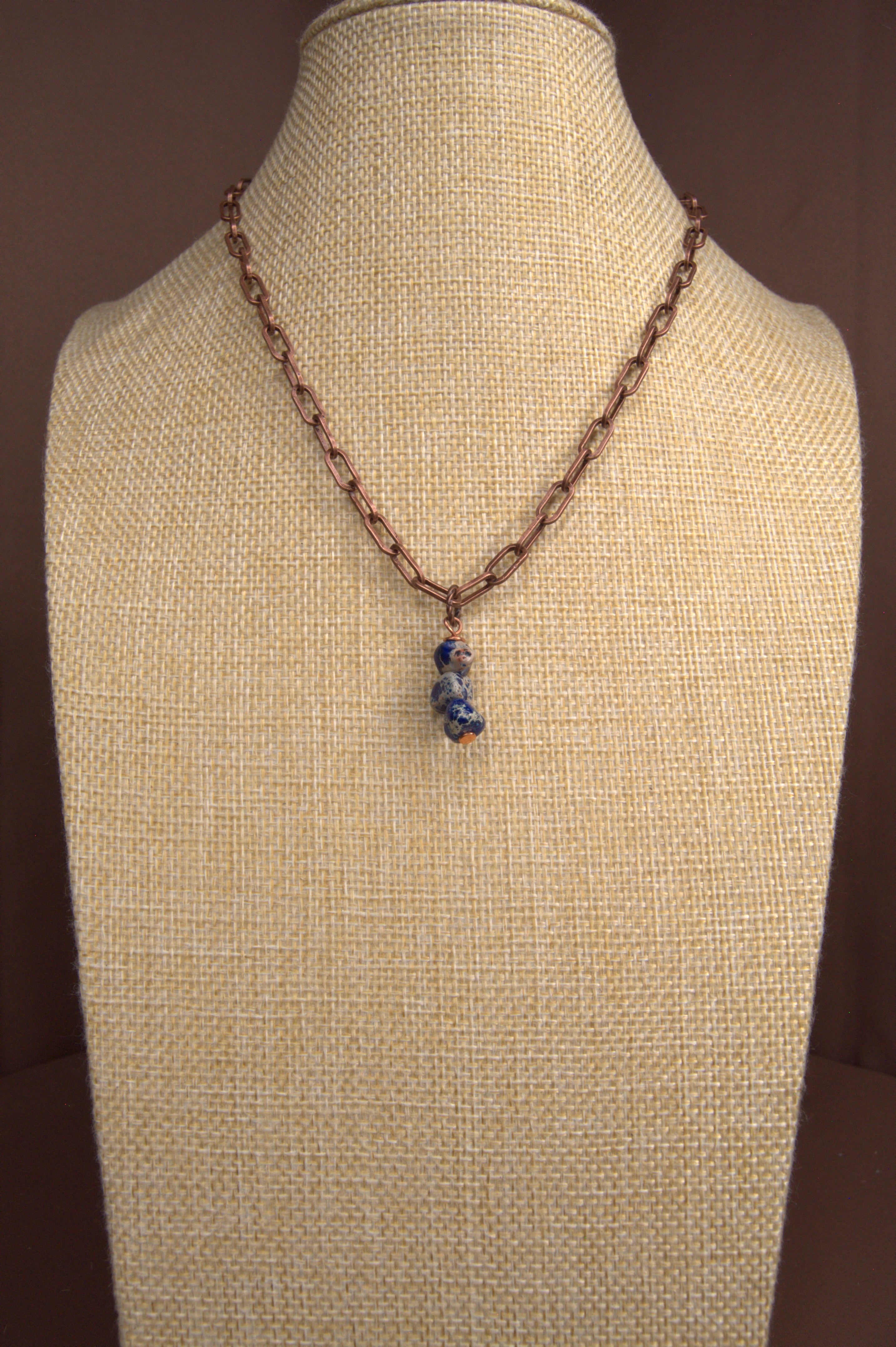 Necklace with a blue pendant on a beige mannequin against a brown background