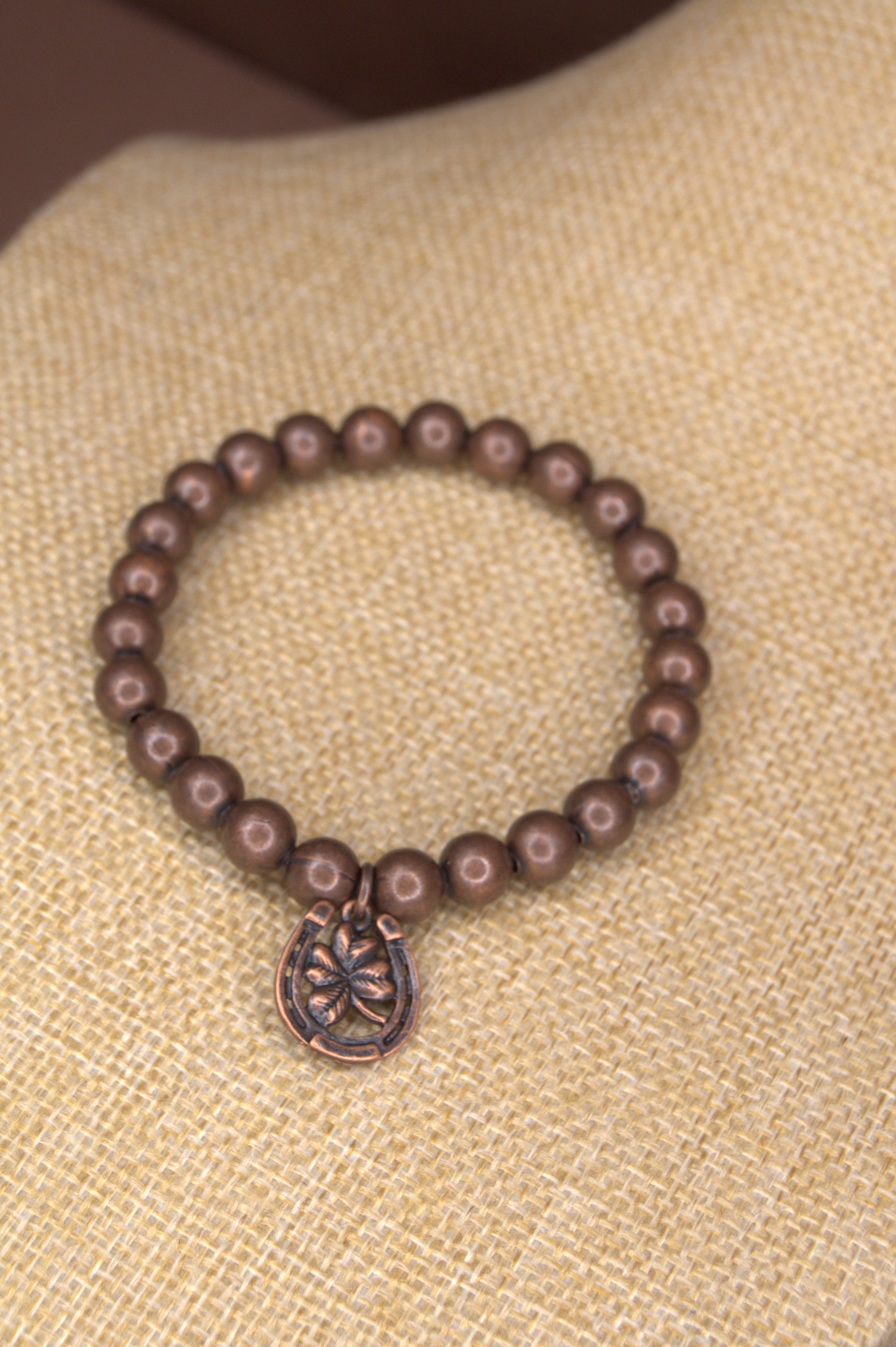 8mm copper metal bead stretch bracelet with a copper horseshoe and clover charm on the bracelet.