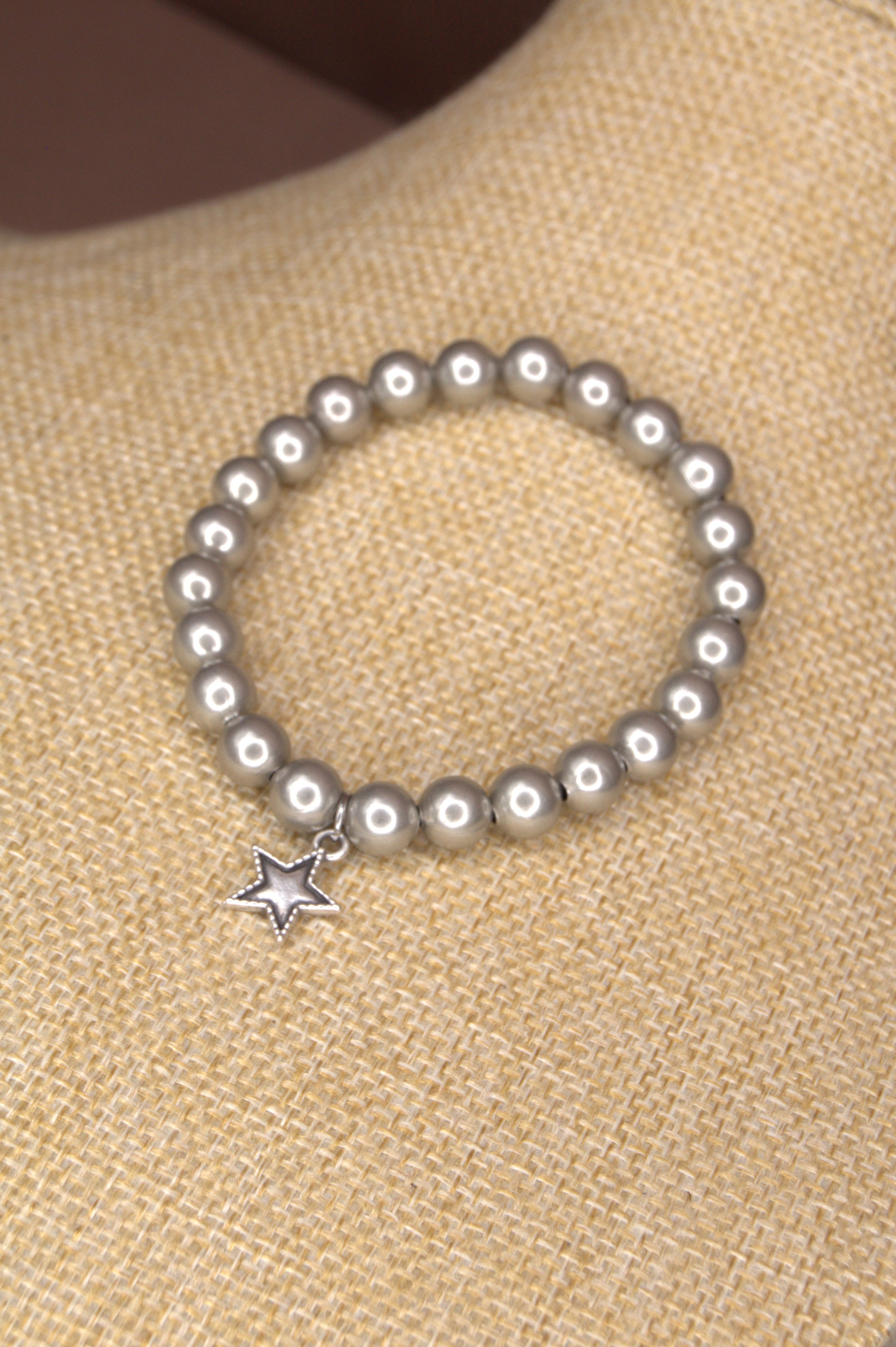 8mm Sliver bead bracelet with a star charm on a beige fabric background