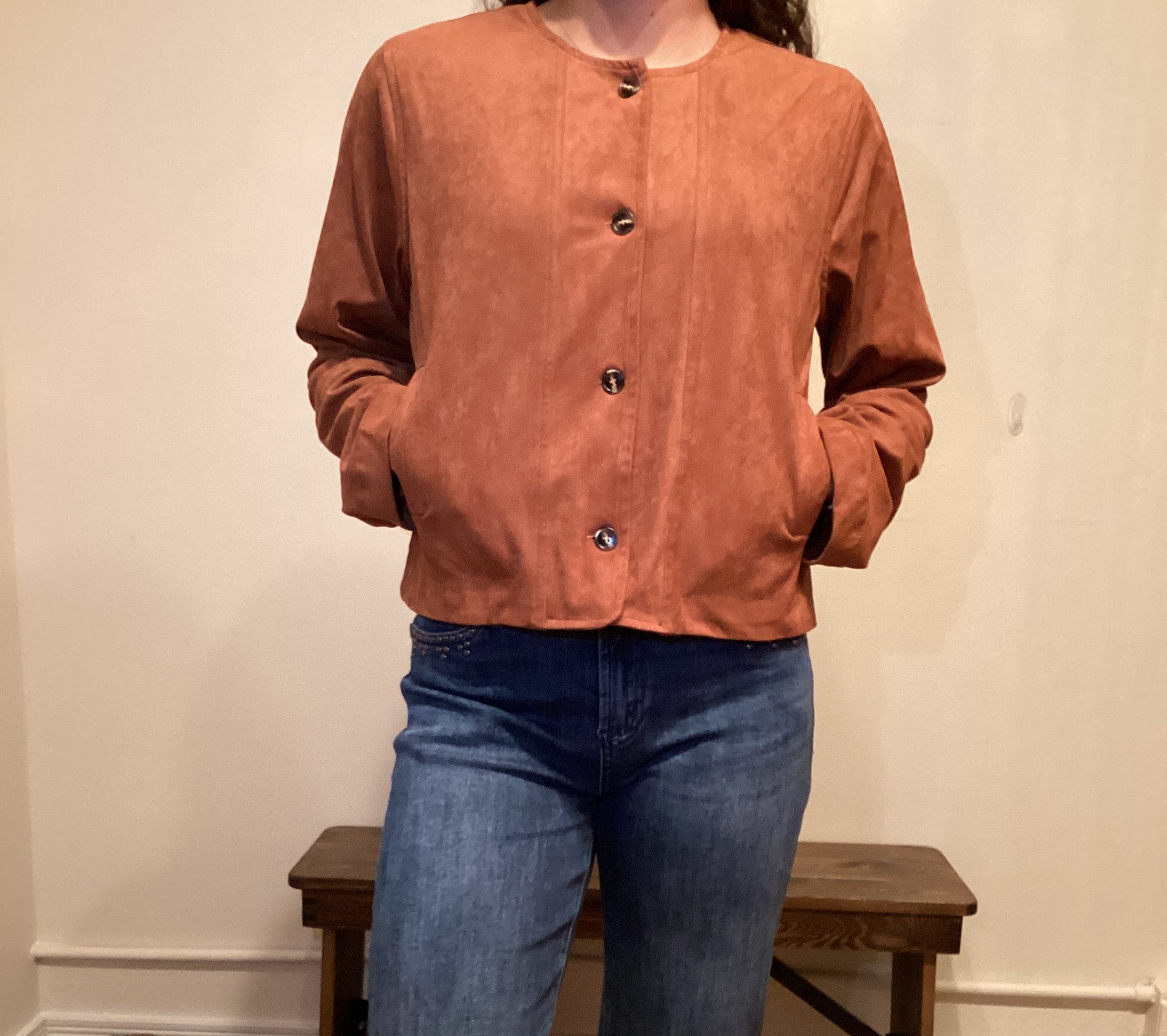 Person wearing a brown faux leather button up jacket and blue jeans